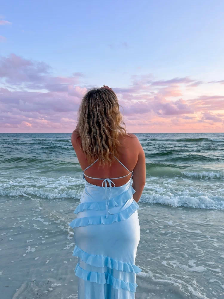 Rear view of a light blue maxi dress with criss-cross back straps, tie detail, and tiered ruffles
