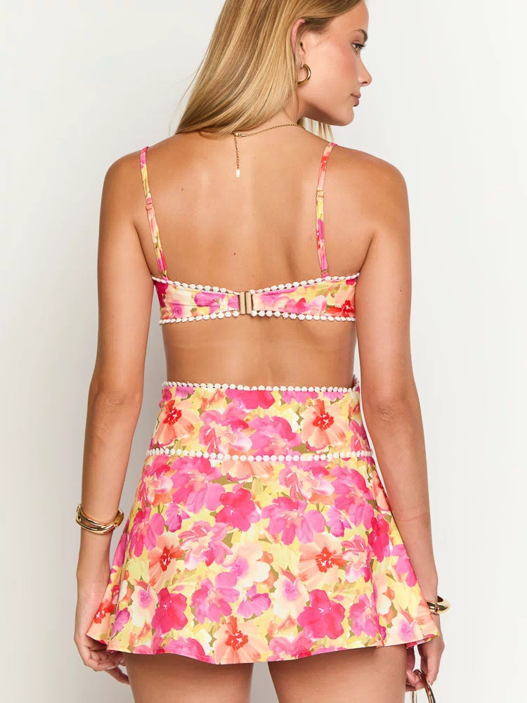 Rear view of the yellow floral mini dress with a hook-and-eye closure and white pom pom trim along the bodice and waist cut-out