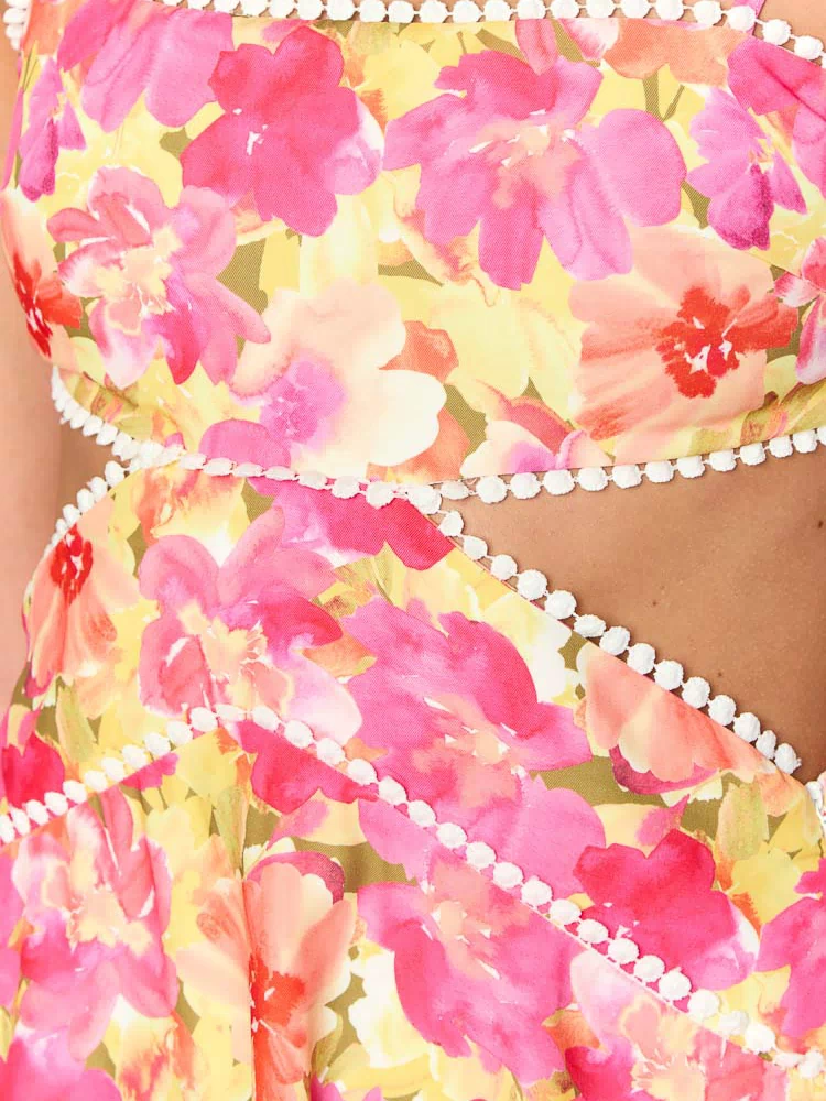 Close-up of the white pom-pom trim detailing the straight neckline and waist cutouts of the yellow floral mini dress