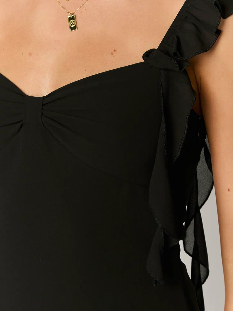 Close-up of the ruffled shoulder strap and ruched sweetheart neckline on a black chiffon mini dress