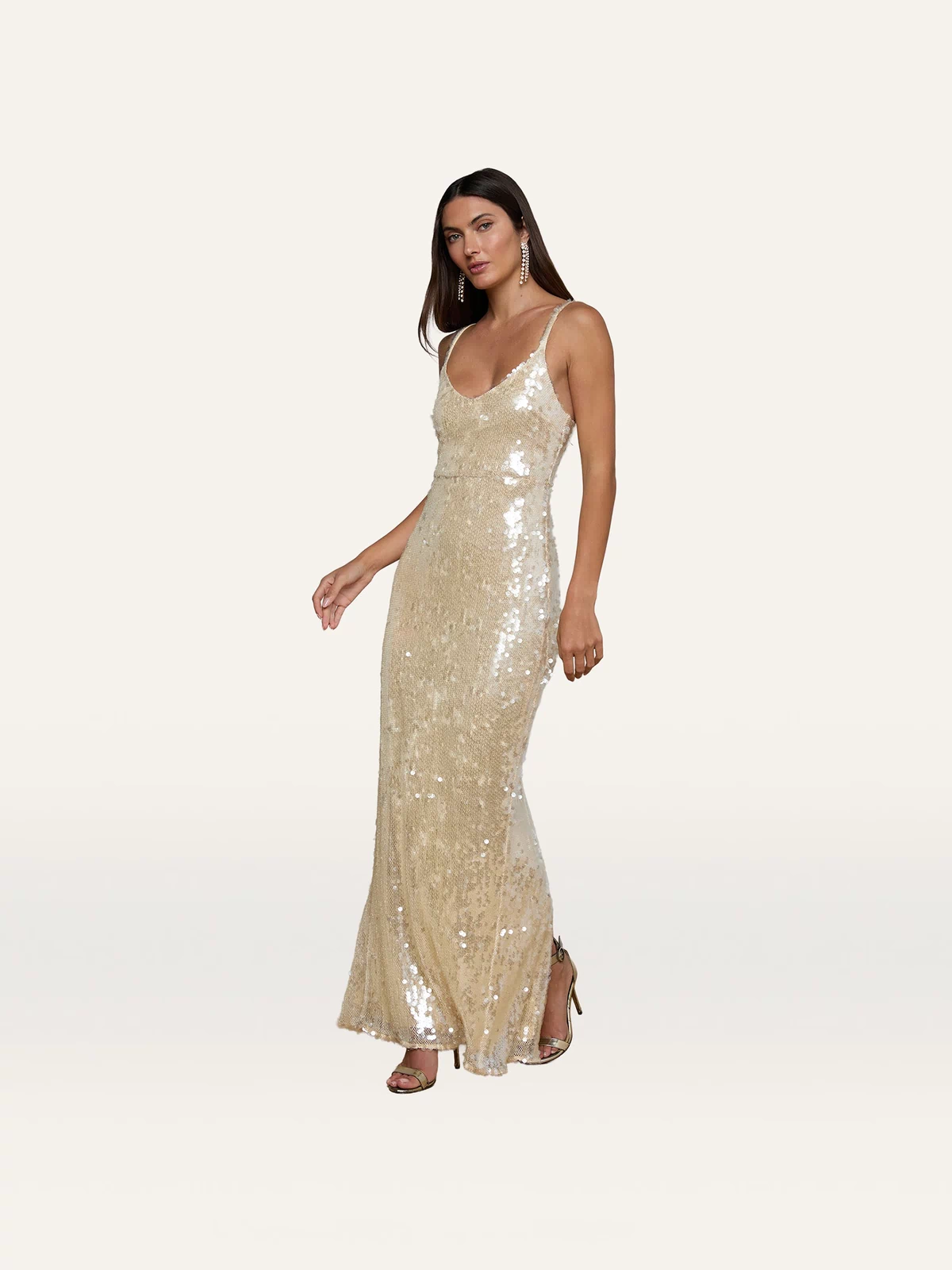 Wearing the dazzling, sleeveless Karma Sequin Maxi Dress with delicate spaghetti straps and high heels, she poses against a plain white background—an elegant look ideal for NYFW 2026.