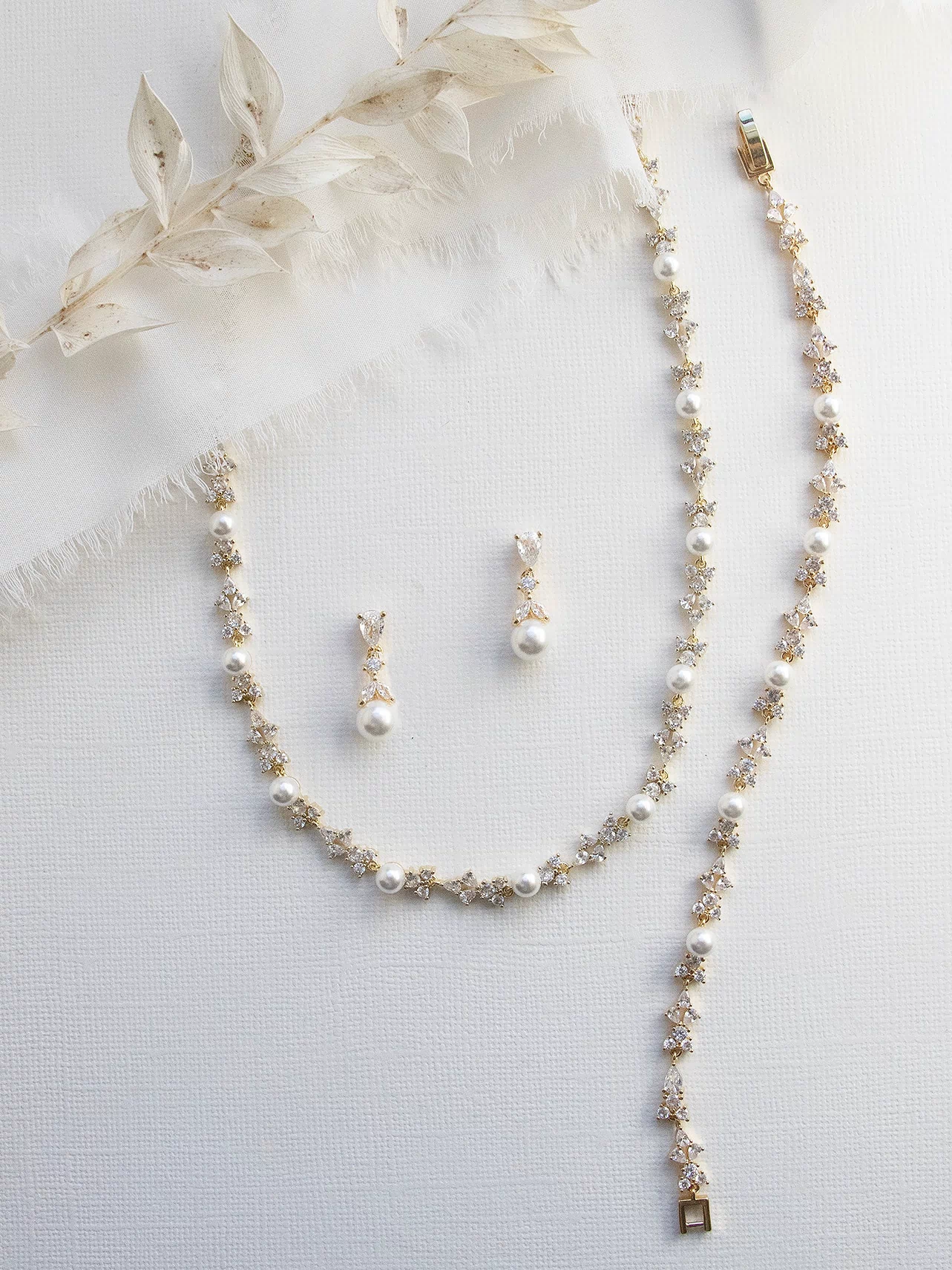 A delicate necklace with a long chain and a pair of earrings with pearls are displayed on a white background.