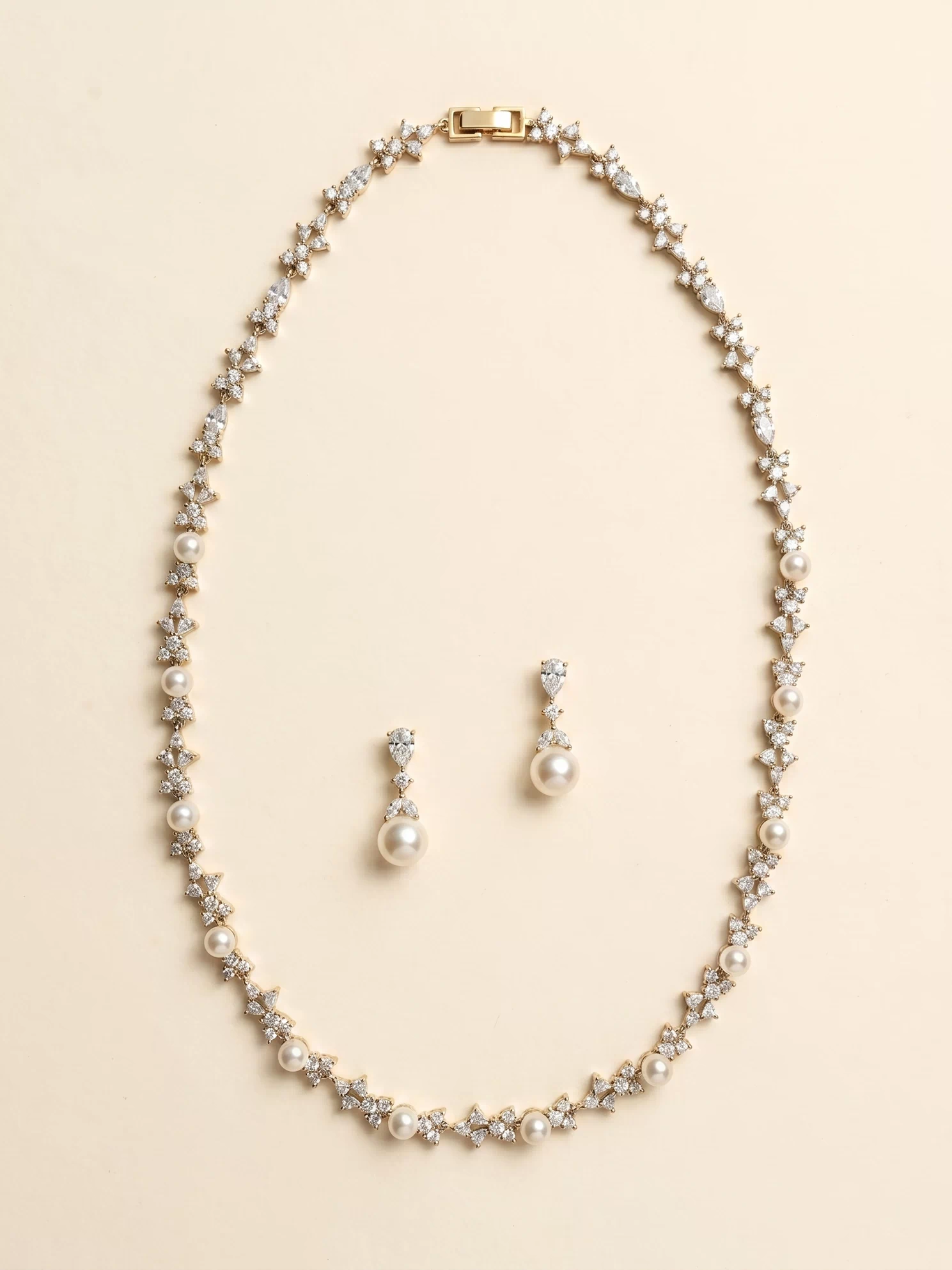 A gold necklace and earrings set are displayed against a light beige background.