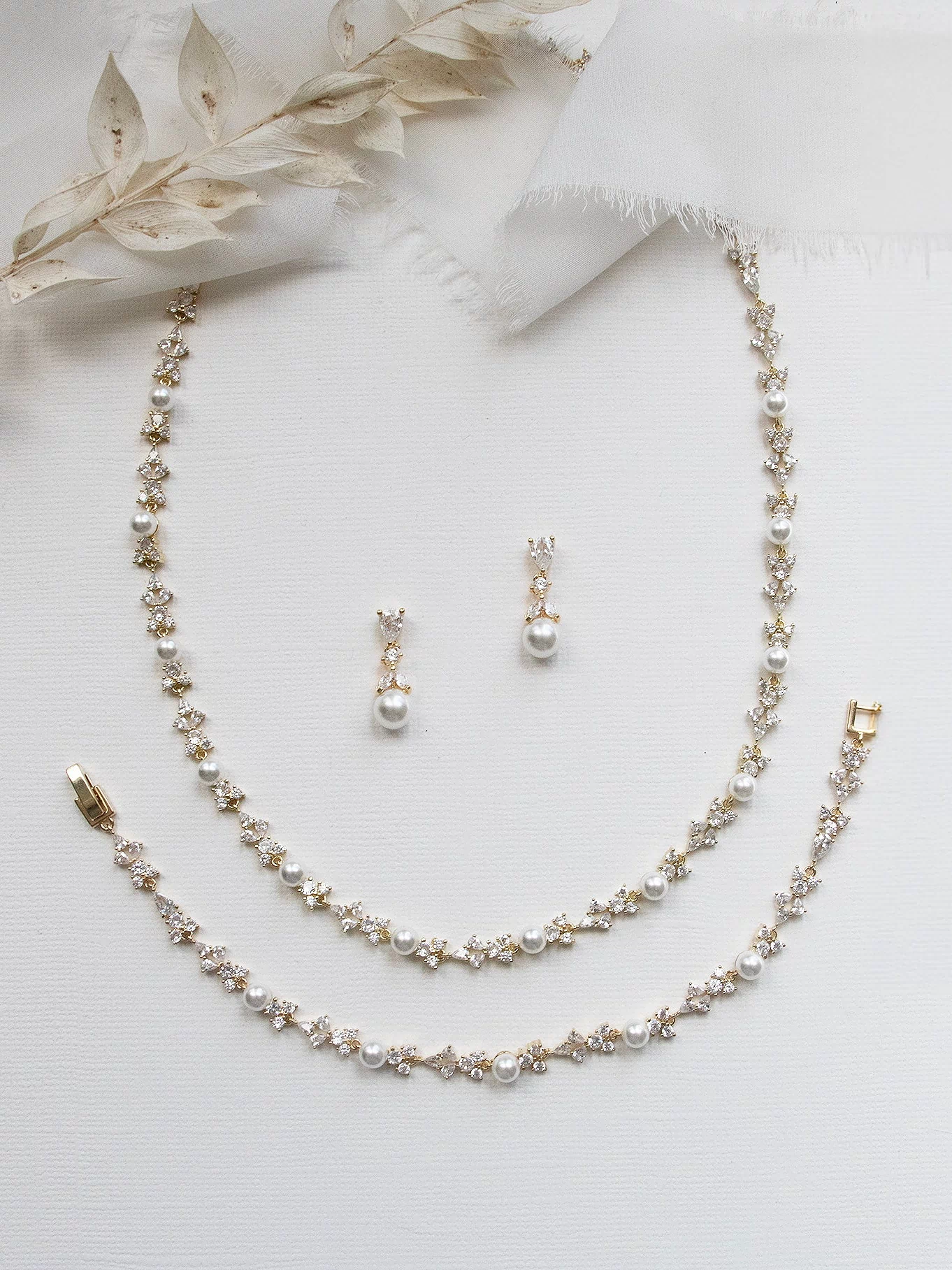 A delicate gold necklace, earrings, and bracelet are arranged on a white background, creating an elegant and sophisticated display.