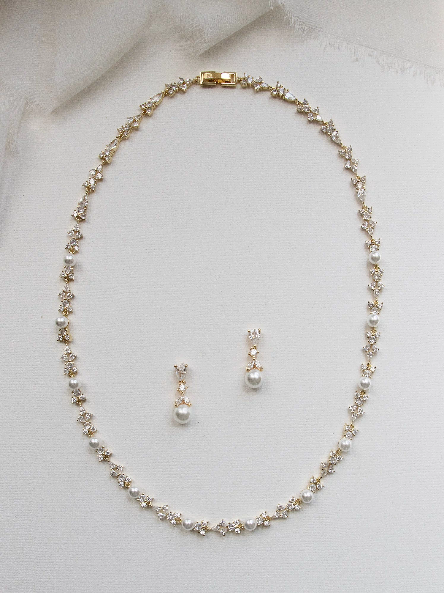 A delicate gold necklace with a row of small pearls and two dangling earrings are displayed on a white background.