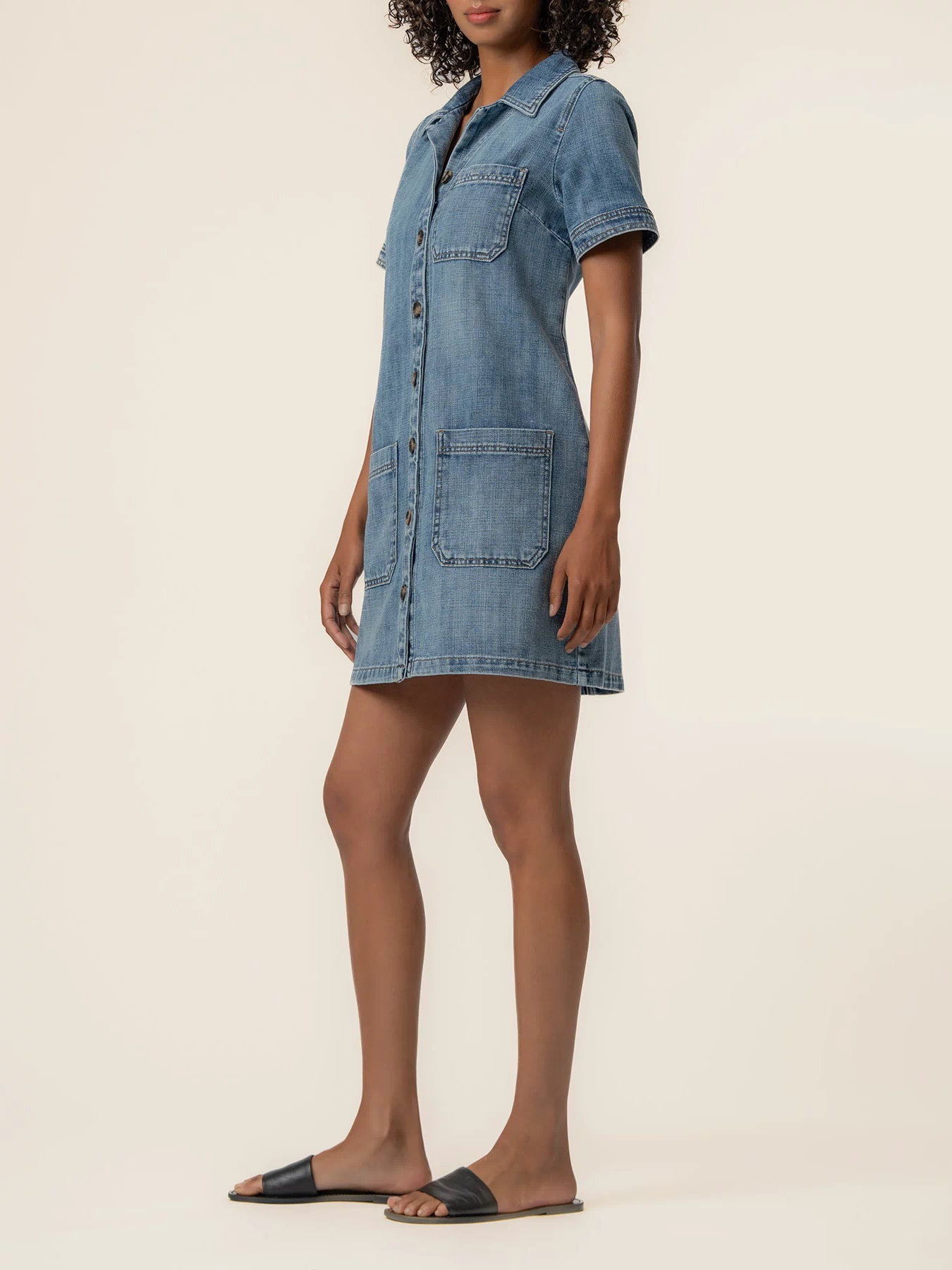 Woman wearing light blue denim shirt dress with short sleeves, chest and front pockets, button front closure.