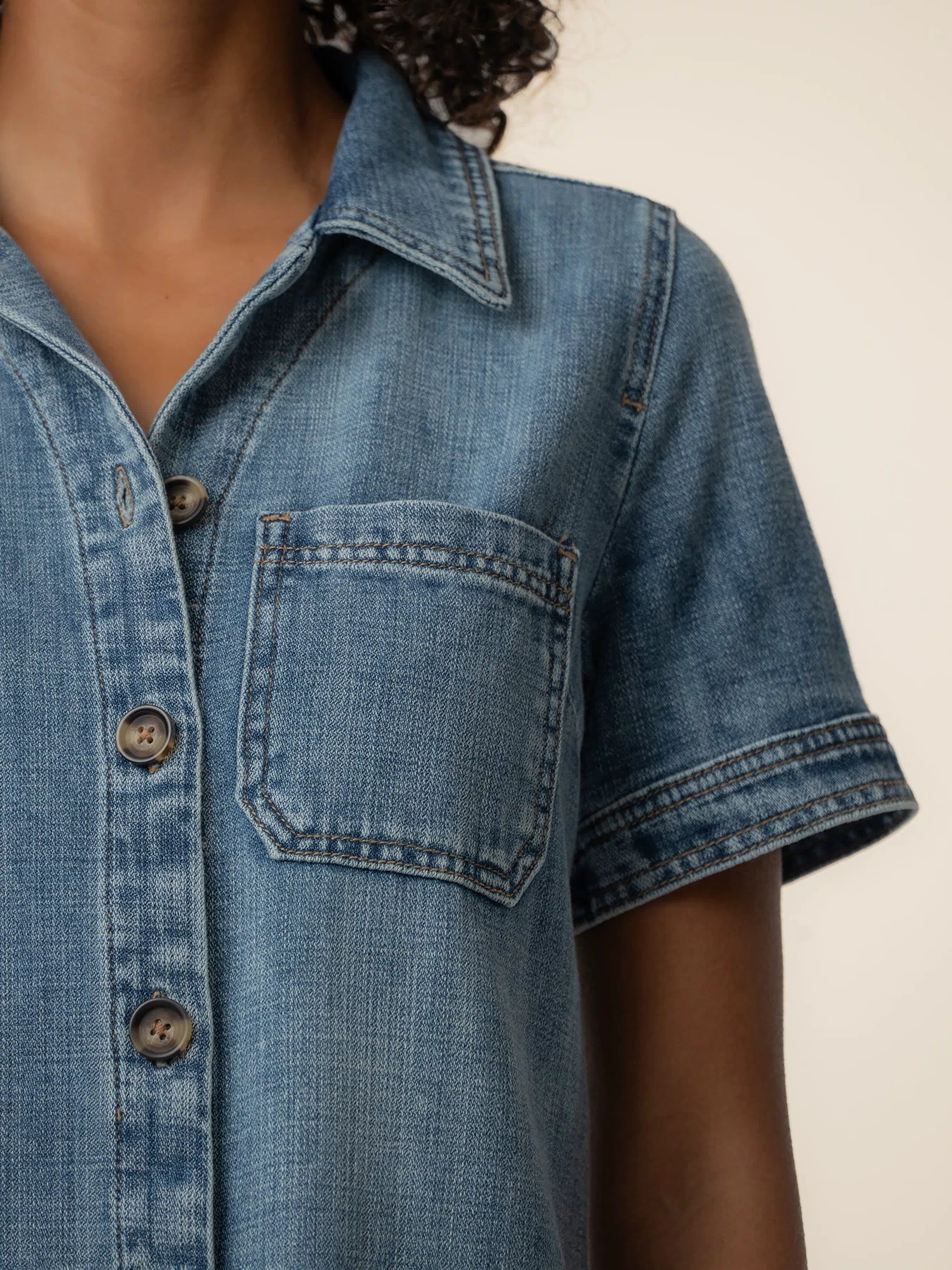 Light blue denim dress with short sleeves, collar, front button closure, and chest pocket with contrast stitching.