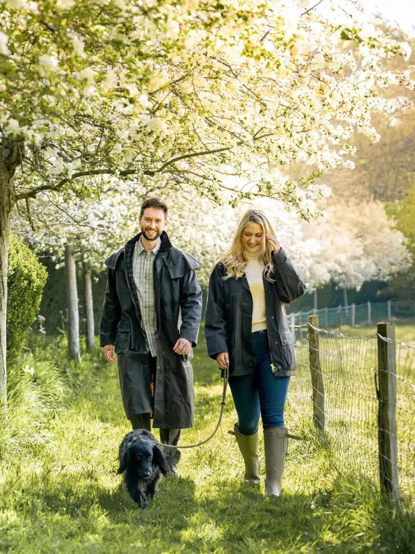 Couple in a traditional wax jacket walking a dog under blooming trees in the park