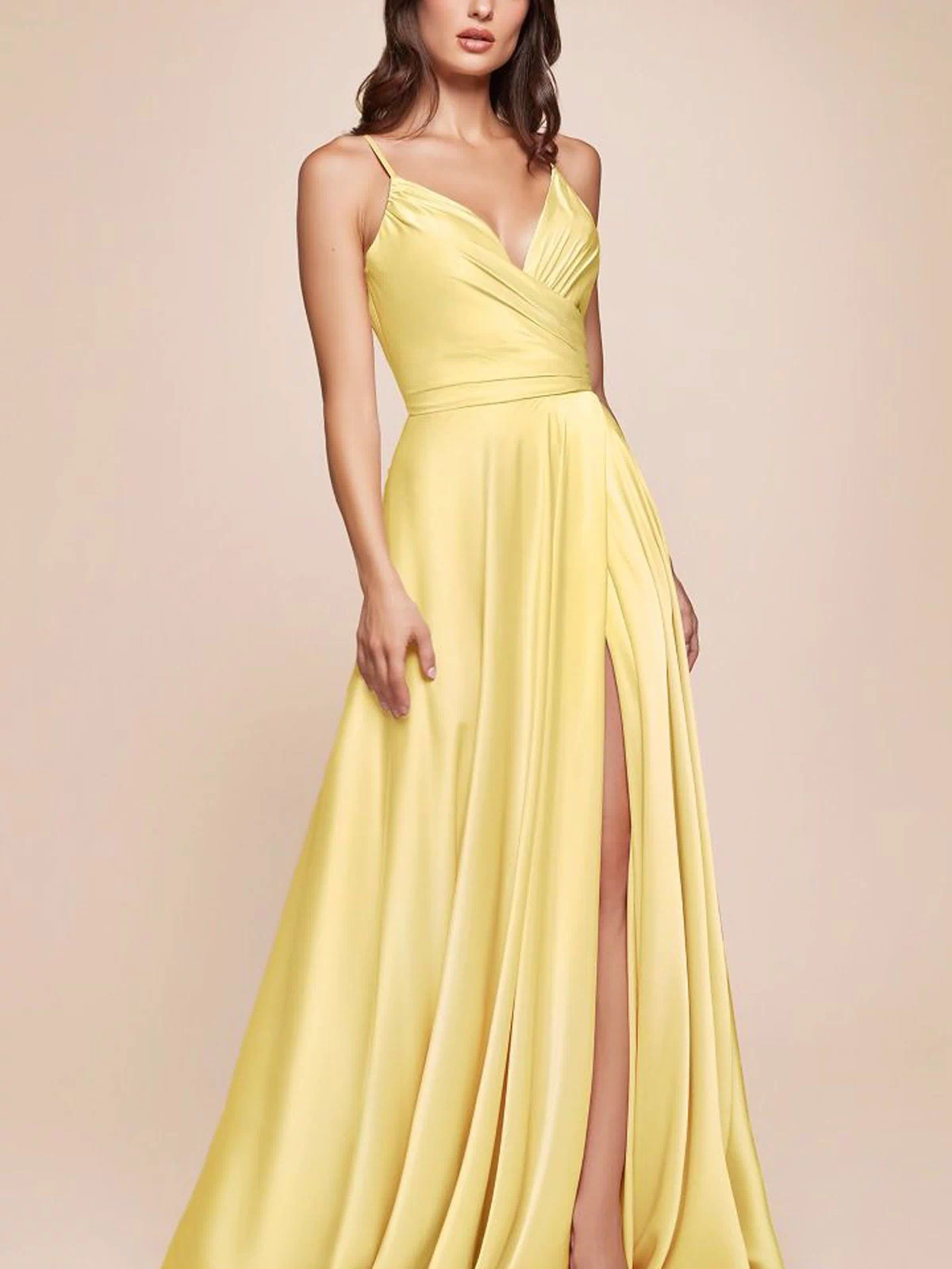 A woman models the Ladivine 7485 Classic Long Satin Formal Prom Dress, a sleeveless yellow gown with a wrap bodice and high slit, against a plain beige background.