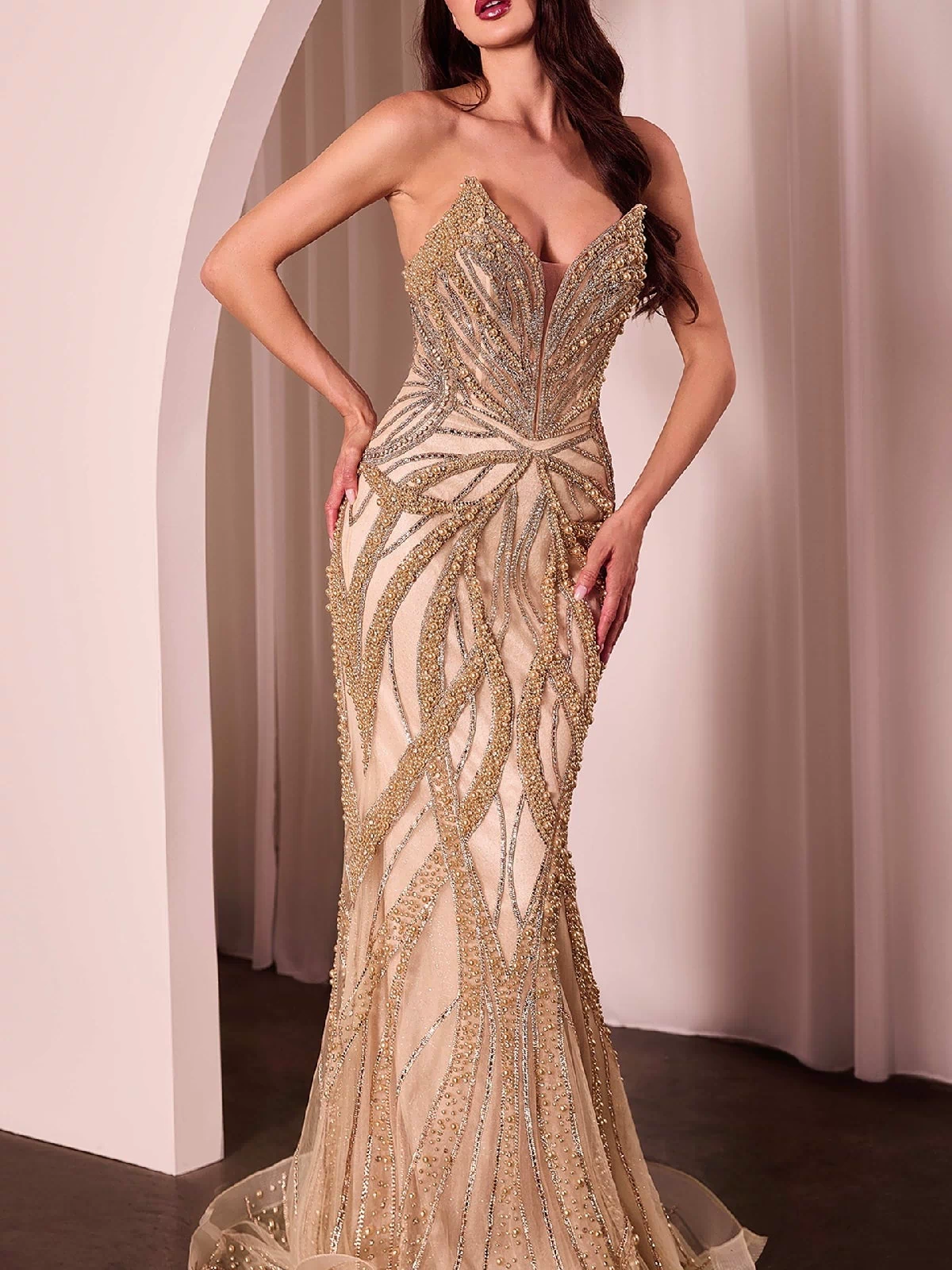 A woman models the Strapless Long Beaded Prom Dress: Ladivine CC0688, showcasing its corset bodice and floor-length beaded design as she stands indoors near an arched doorway with draped white curtains.