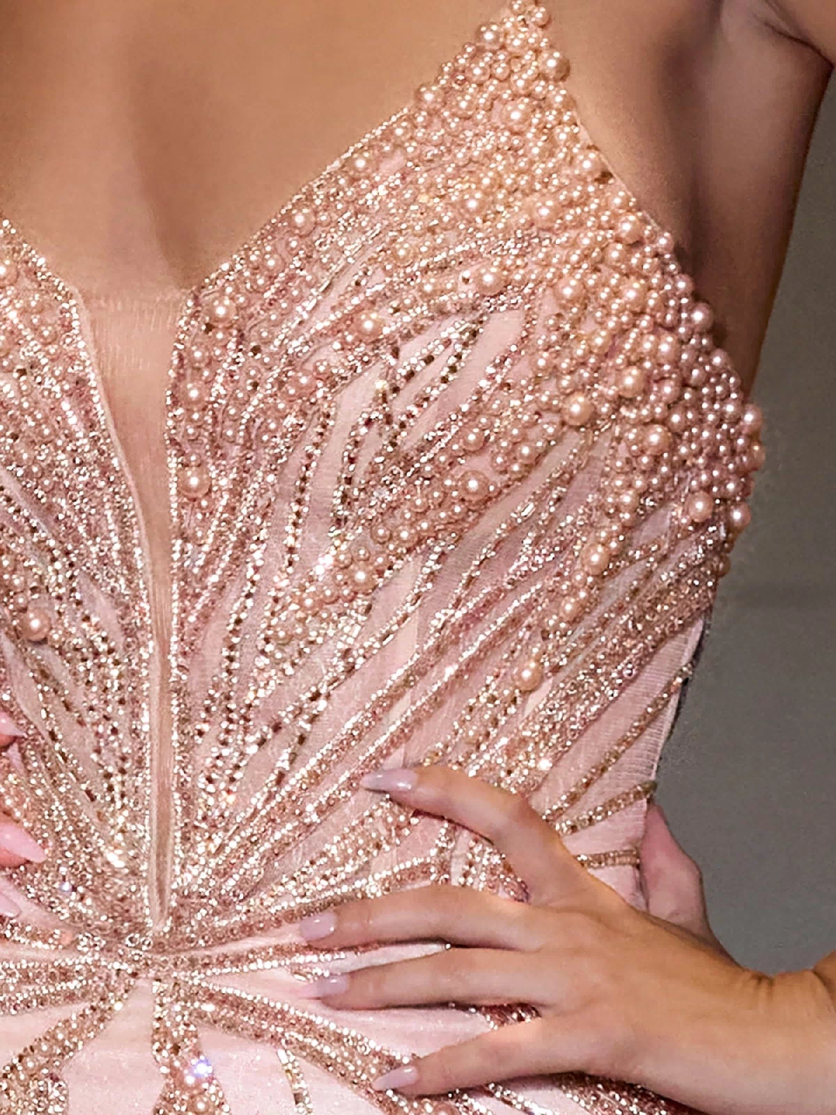 A person poses confidently in the Ladivine CC0688, a strapless long beaded prom dress with a corset bodice and blush pink color, embellished with pearls.