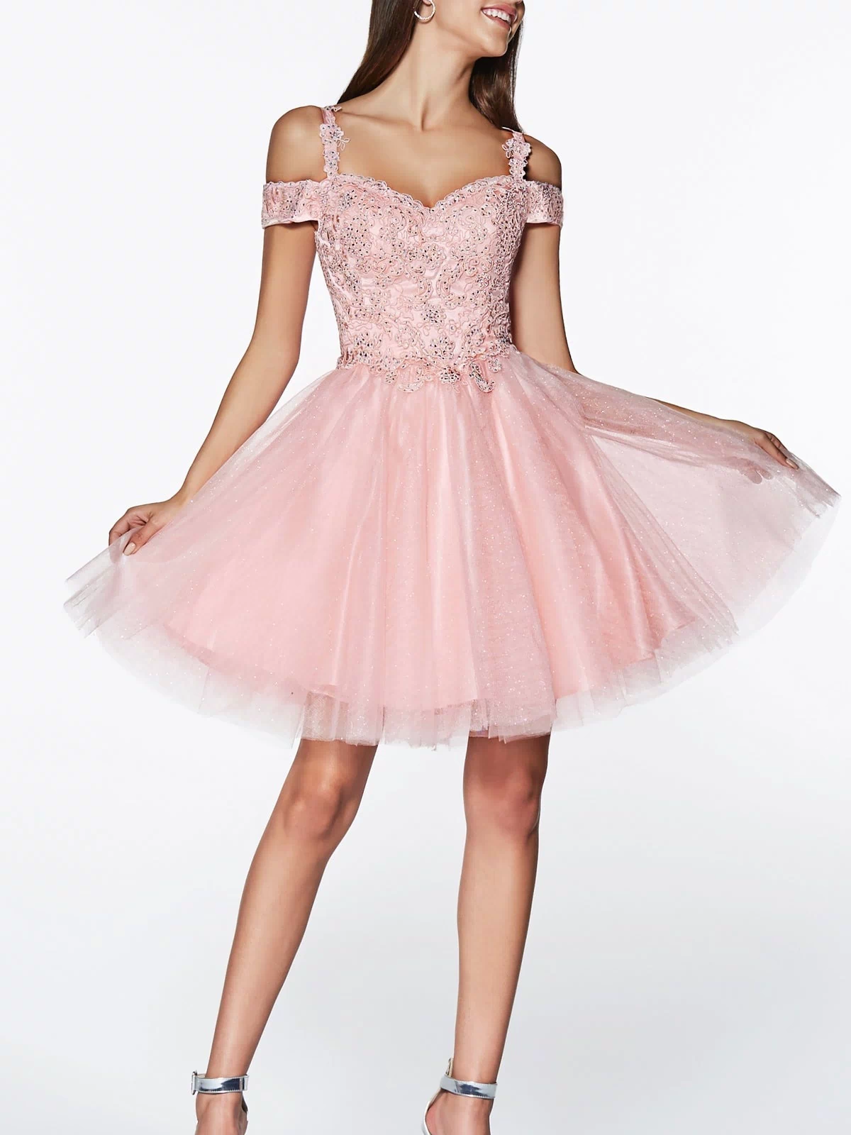 A woman wears the Cold-Shoulder Short Glitter Homecoming Dress CD0132, a light pink homecoming dress with lace and tulle details, paired with silver high-heeled sandals.