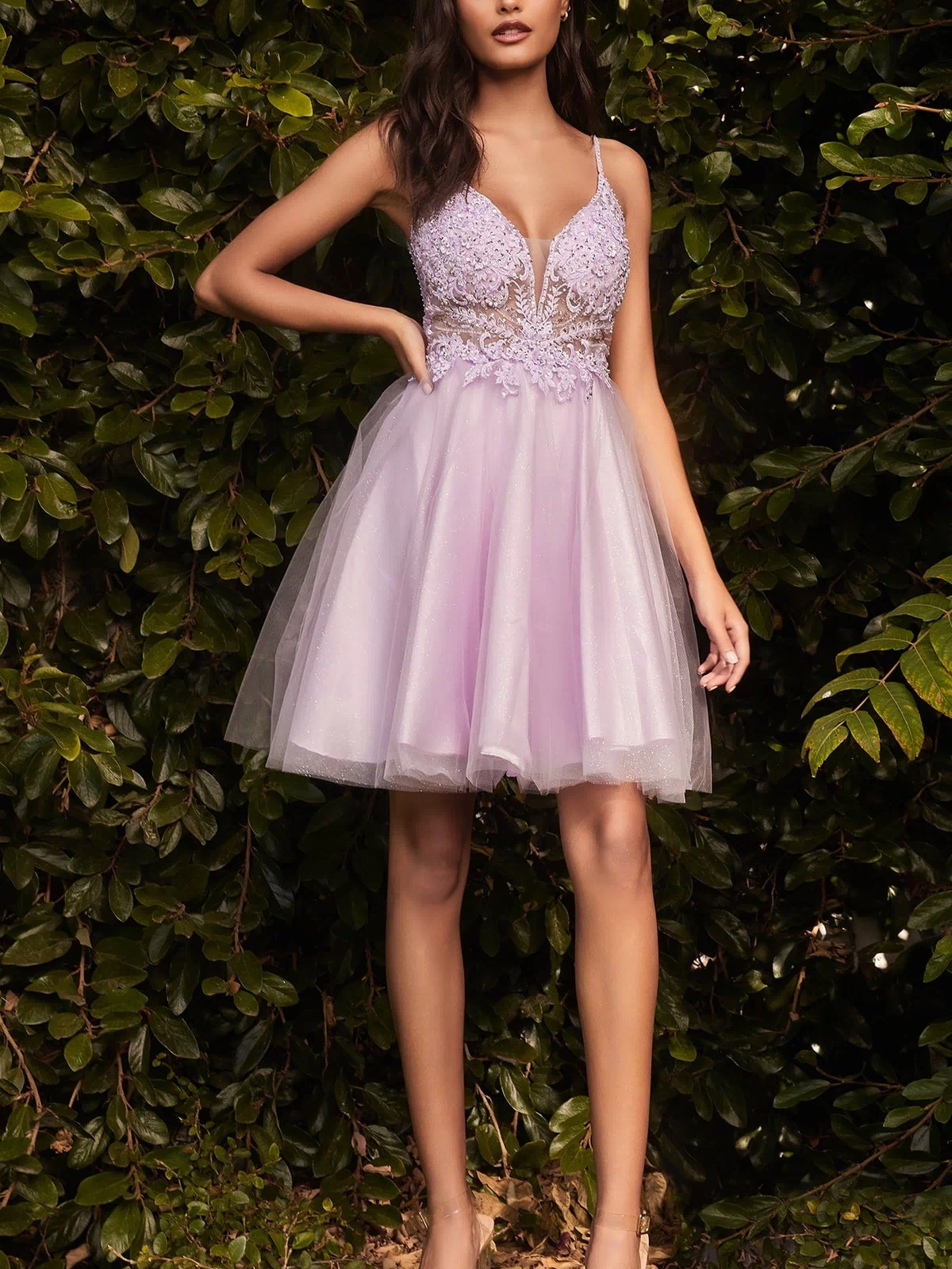 A woman stands outdoors before lush greenery, wearing the Lace-Bodice Short A-Line Homecoming Dress CD0190 with a sheer-lace bodice, lace detailing, and nude high-heeled sandals.