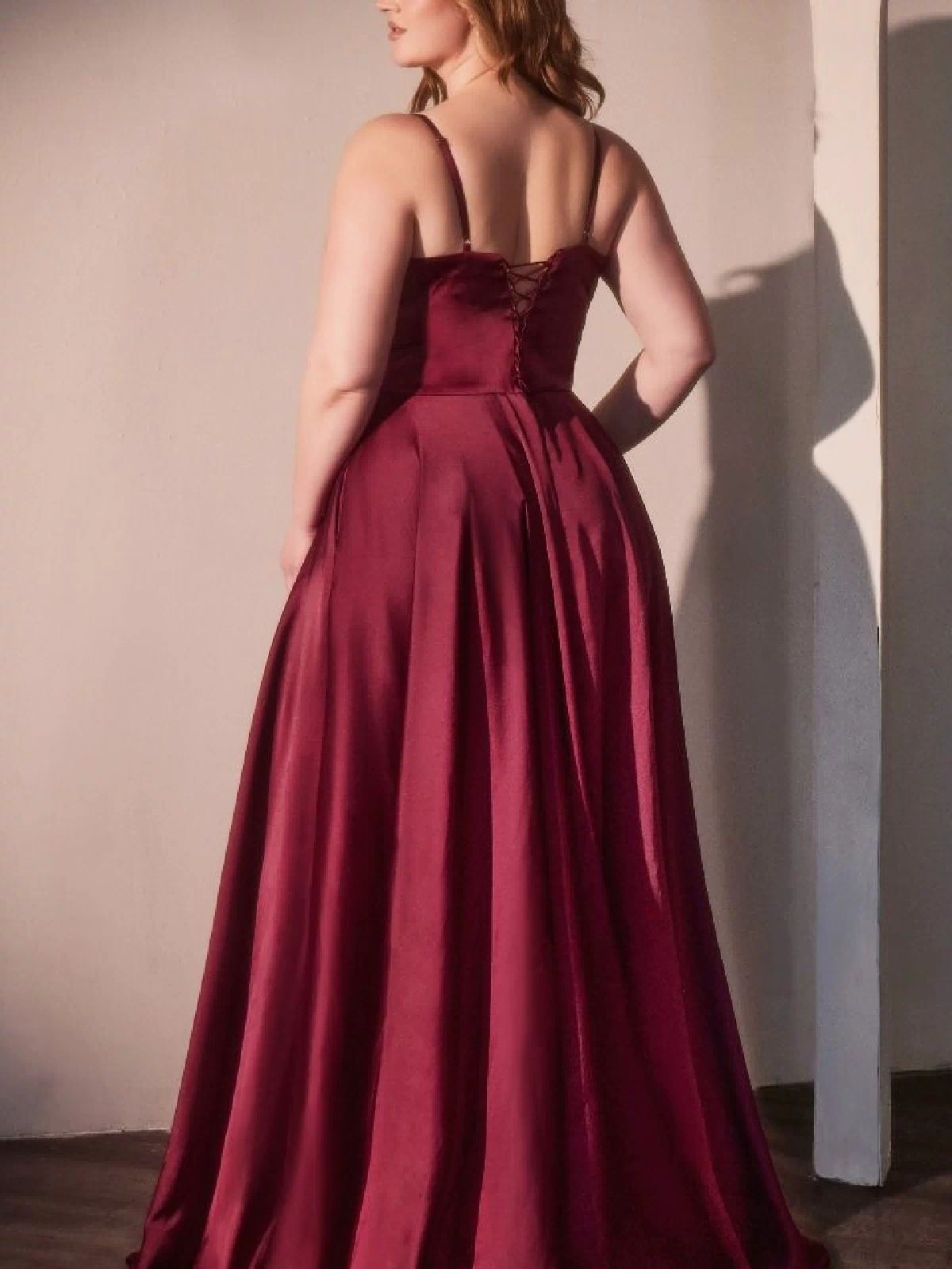 A woman in a sleeveless, floor-length Ladivine CD337C Plus-Size Long A-Line Prom Dress stands with her back to the camera in a softly lit room.