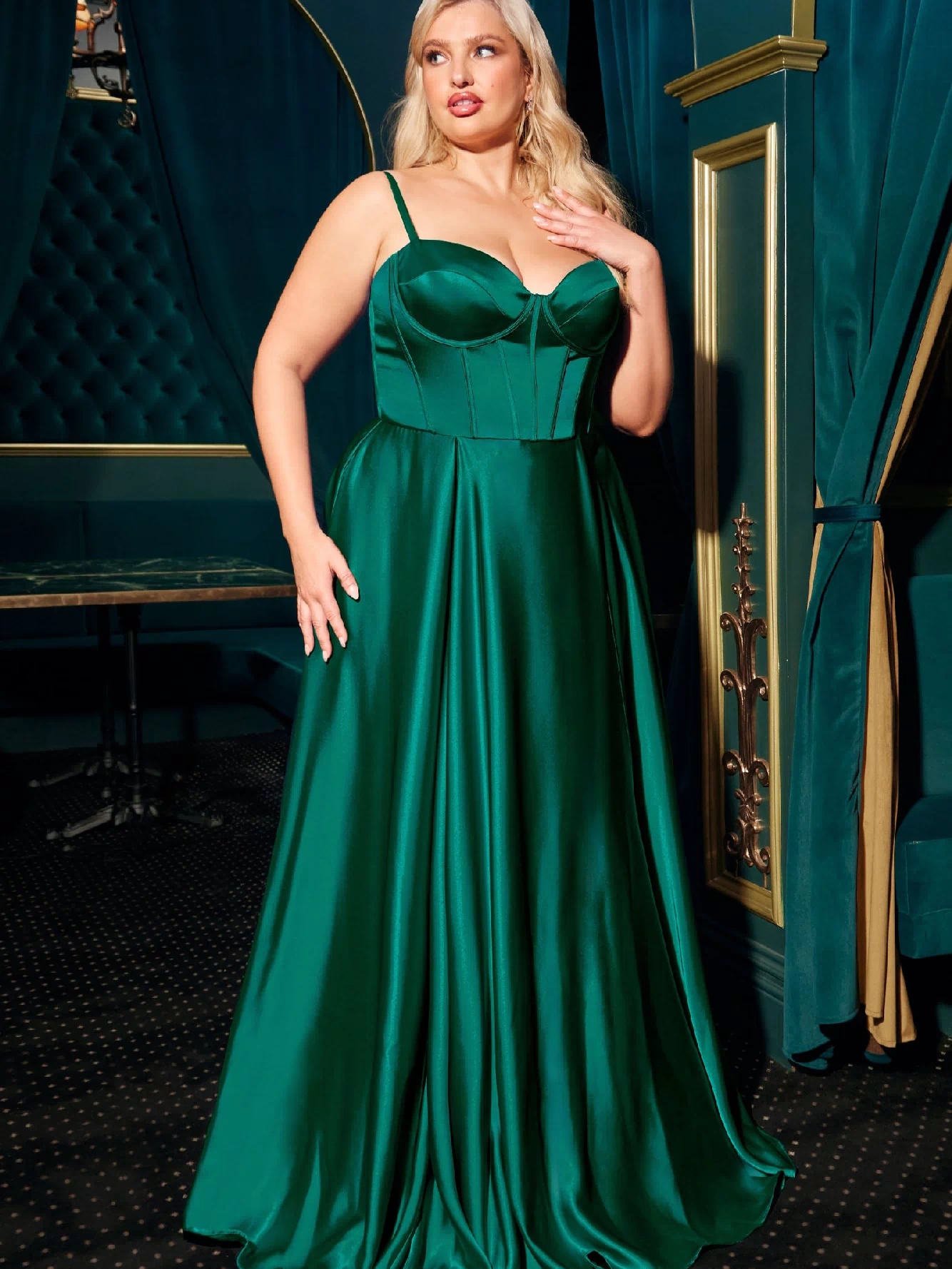 A woman poses gracefully indoors on a dark carpet, wearing the Ladivine CD337C plus-size long A-line emerald green prom dress with thin straps.