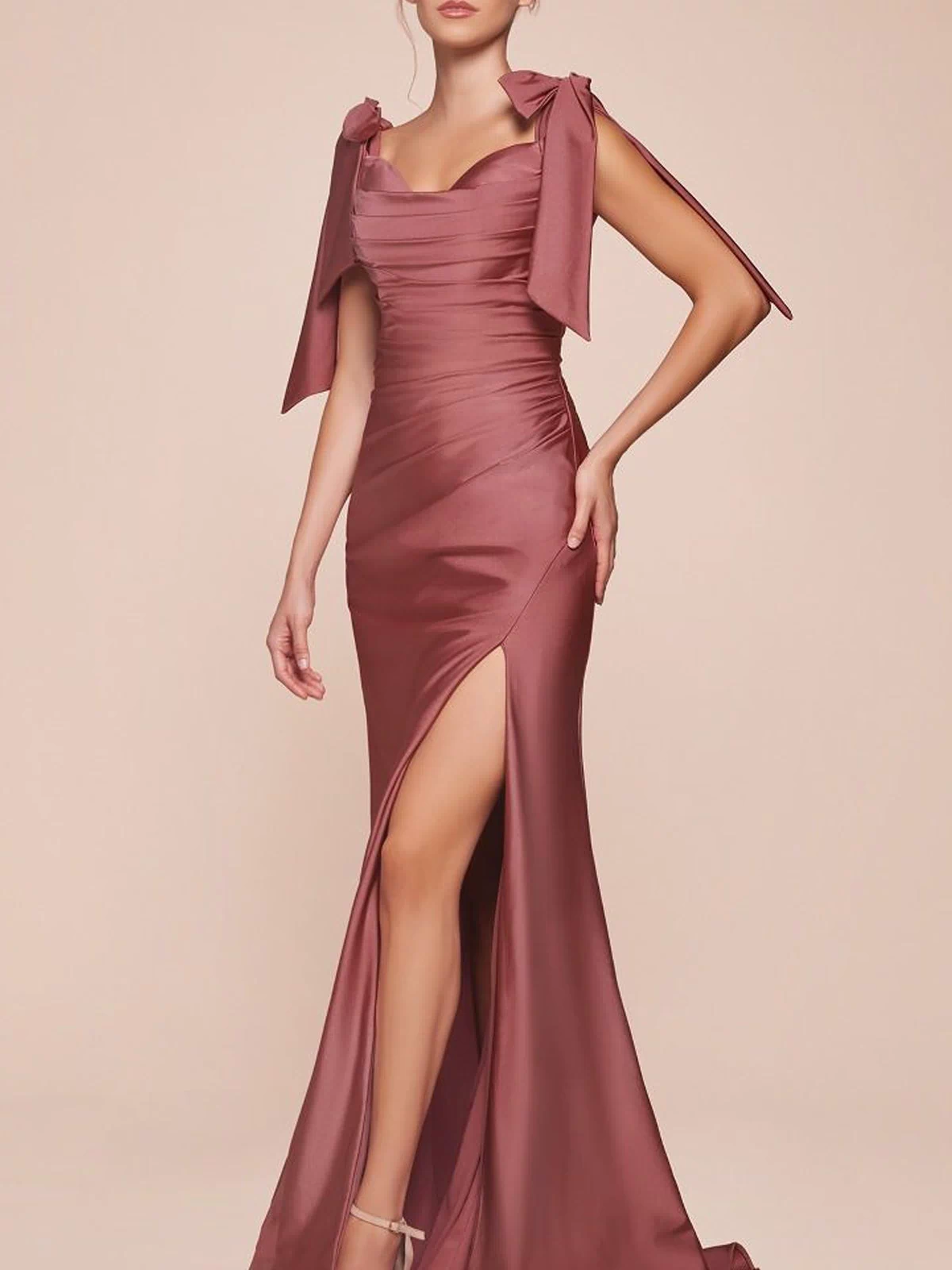 A woman stands against a plain light background wearing the mauve Off-Shoulder Ruched Prom Dress: Ladivine CD943, featuring bow details on the shoulders, a high slit, and a sleek sleeveless floor-length design.