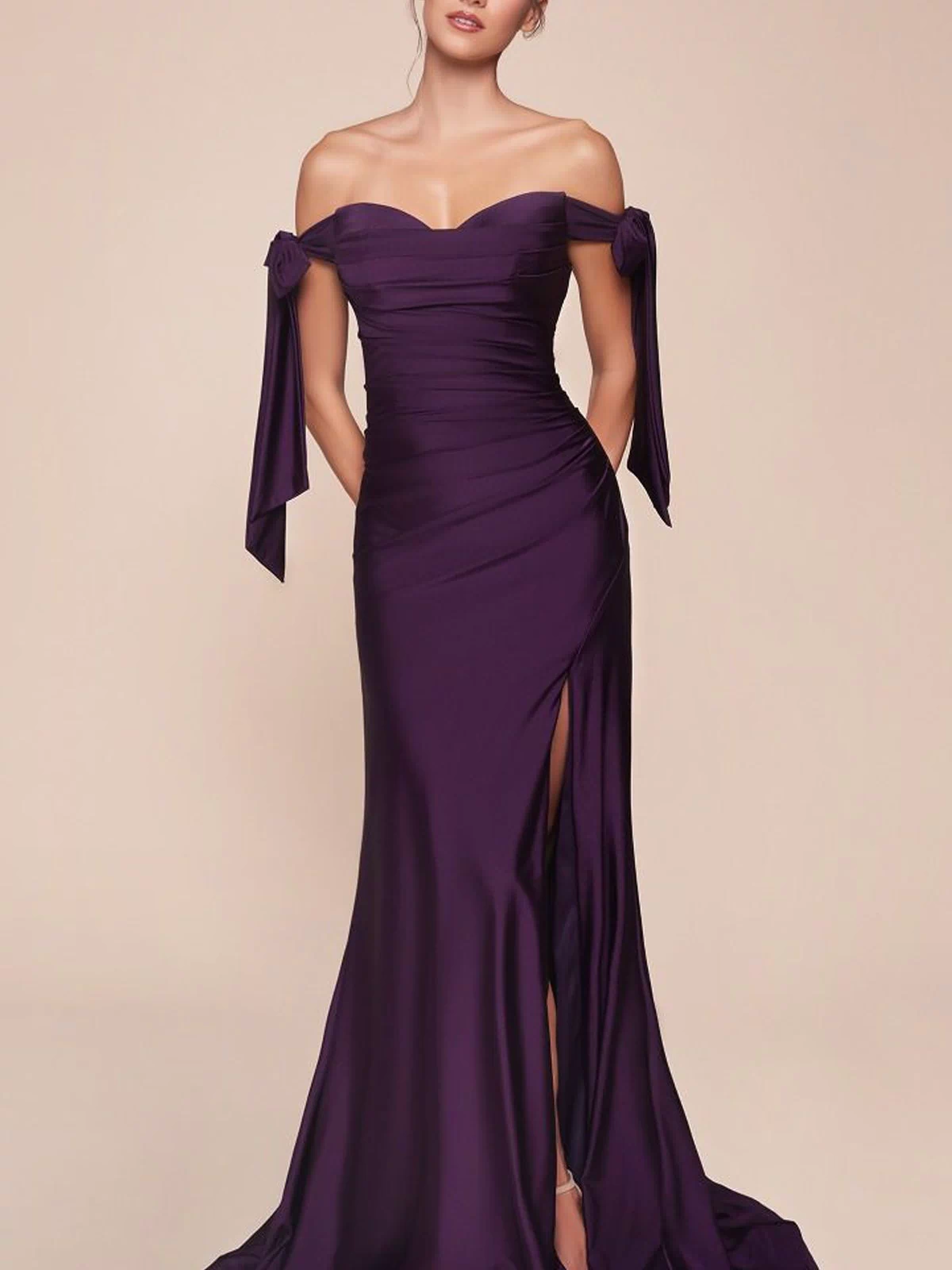 A woman models the Off-Shoulder Ruched Prom Dress: Ladivine CD943 in deep purple stretch jersey, featuring a side slit and sleeve bows, set against a plain beige background.