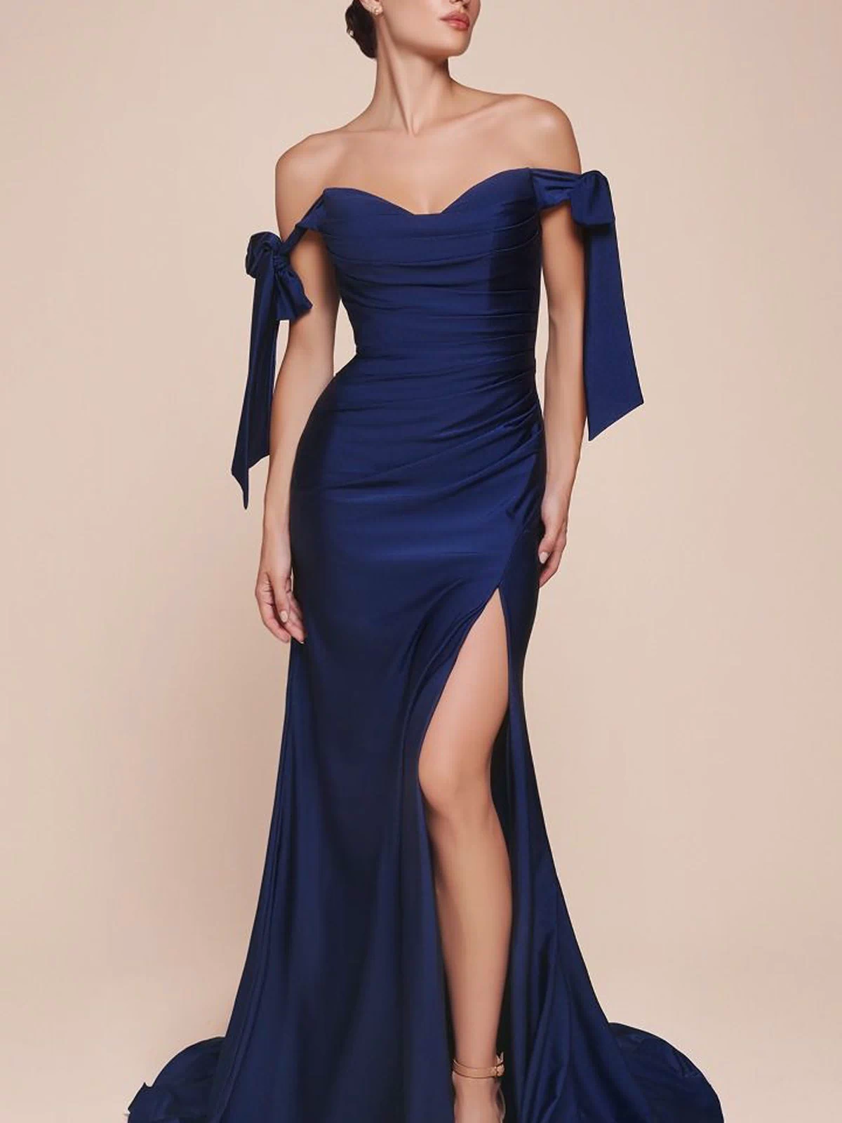 A woman in the navy blue Off-Shoulder Ruched Prom Dress: Ladivine CD943, featuring a fitted silhouette, side bows, and a thigh-high slit, stands against a plain beige background.