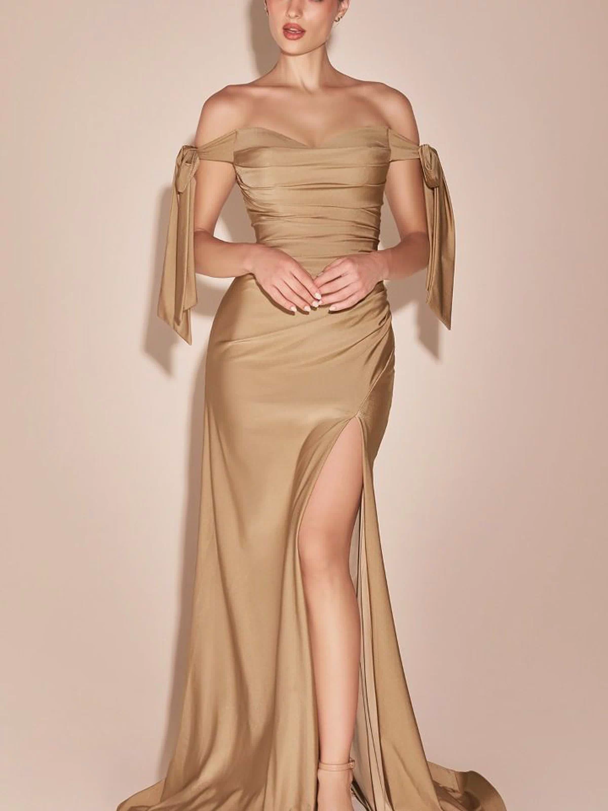 Woman in an elegant Off-Shoulder Ruched Prom Dress: Ladivine CD943 with a gold satin finish, side slit, and bow sleeves, posing against a beige background.