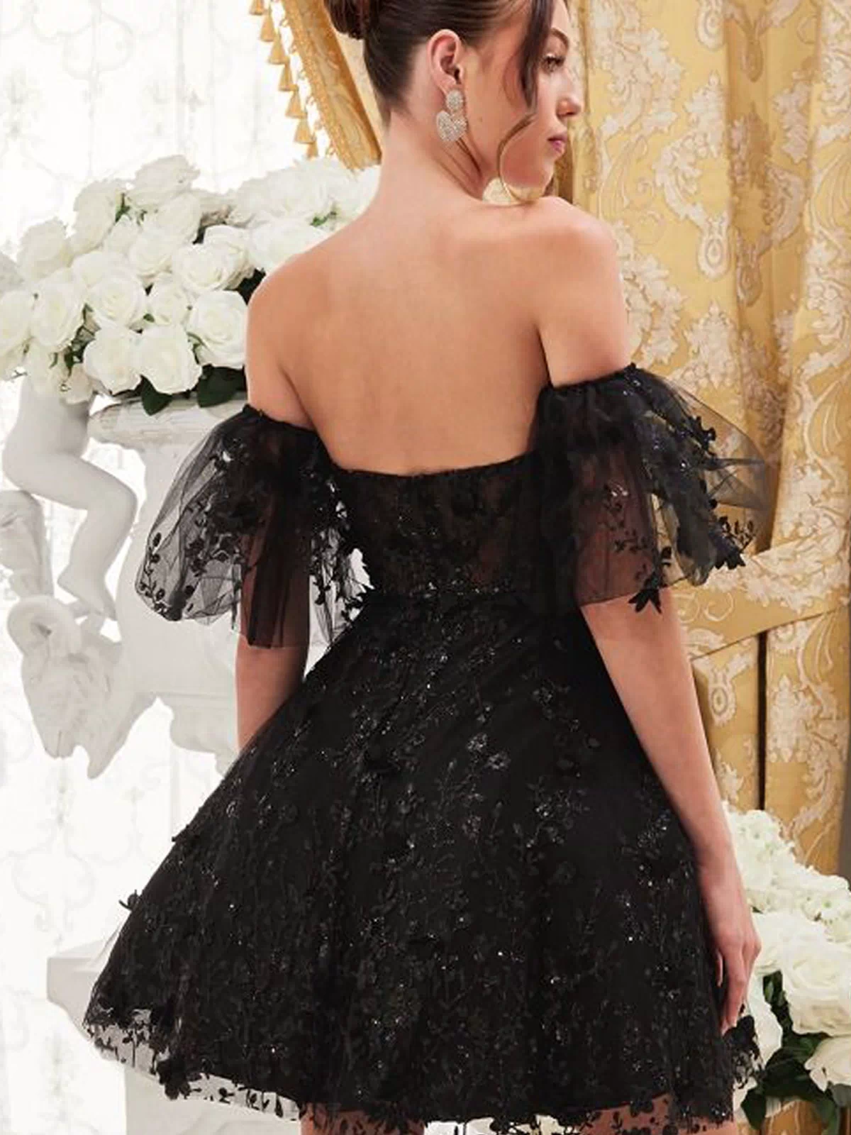 A woman wearing the Puff-Sleeve Short Strapless Homecoming Dress KV1089 stands indoors near white roses and gold curtains, facing away from the camera.