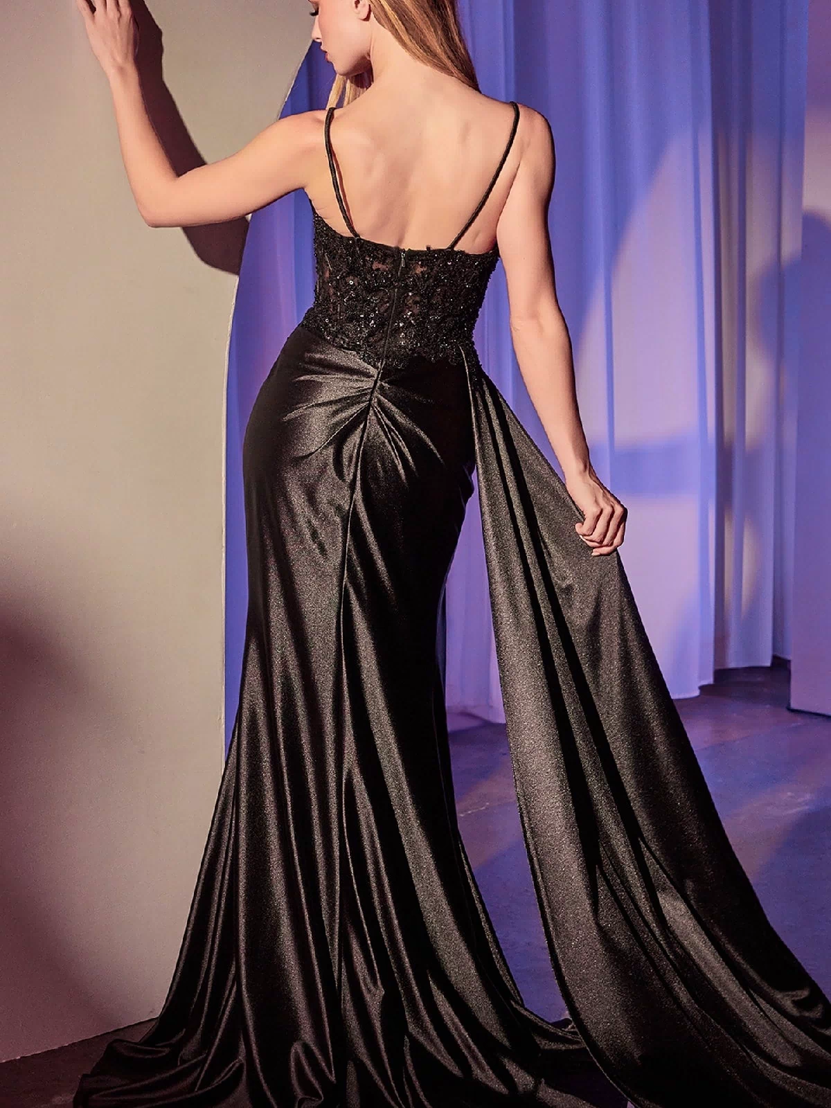 Wearing the Ladivine KV1117 Side-Sash Long Satin Prom Dress, a woman stands with her back to us, gracefully holding the train of her elegant gown, which features a beaded-lace bodice.