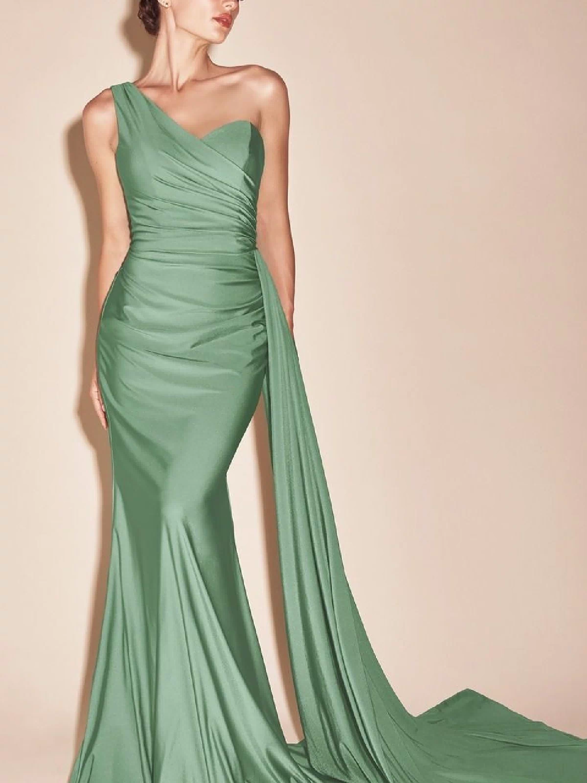 A woman wears the Side-Sash One-Shoulder Long Prom Dress PT004 in sage green, featuring a fitted silhouette and a long draped sash, standing against a plain beige background.