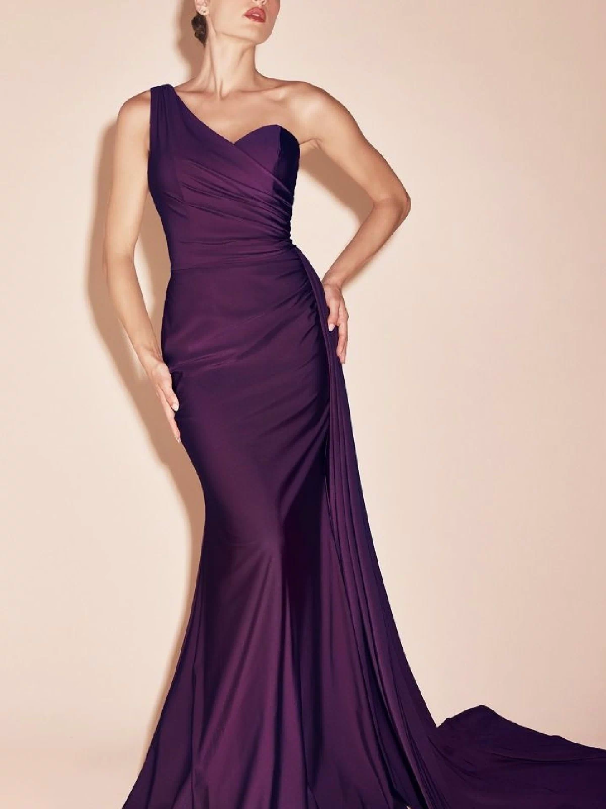Woman modeling the Side-Sash One-Shoulder Long Prom Dress PT004 in dark purple, featuring a fitted silhouette and long train, stands against a simple light background.