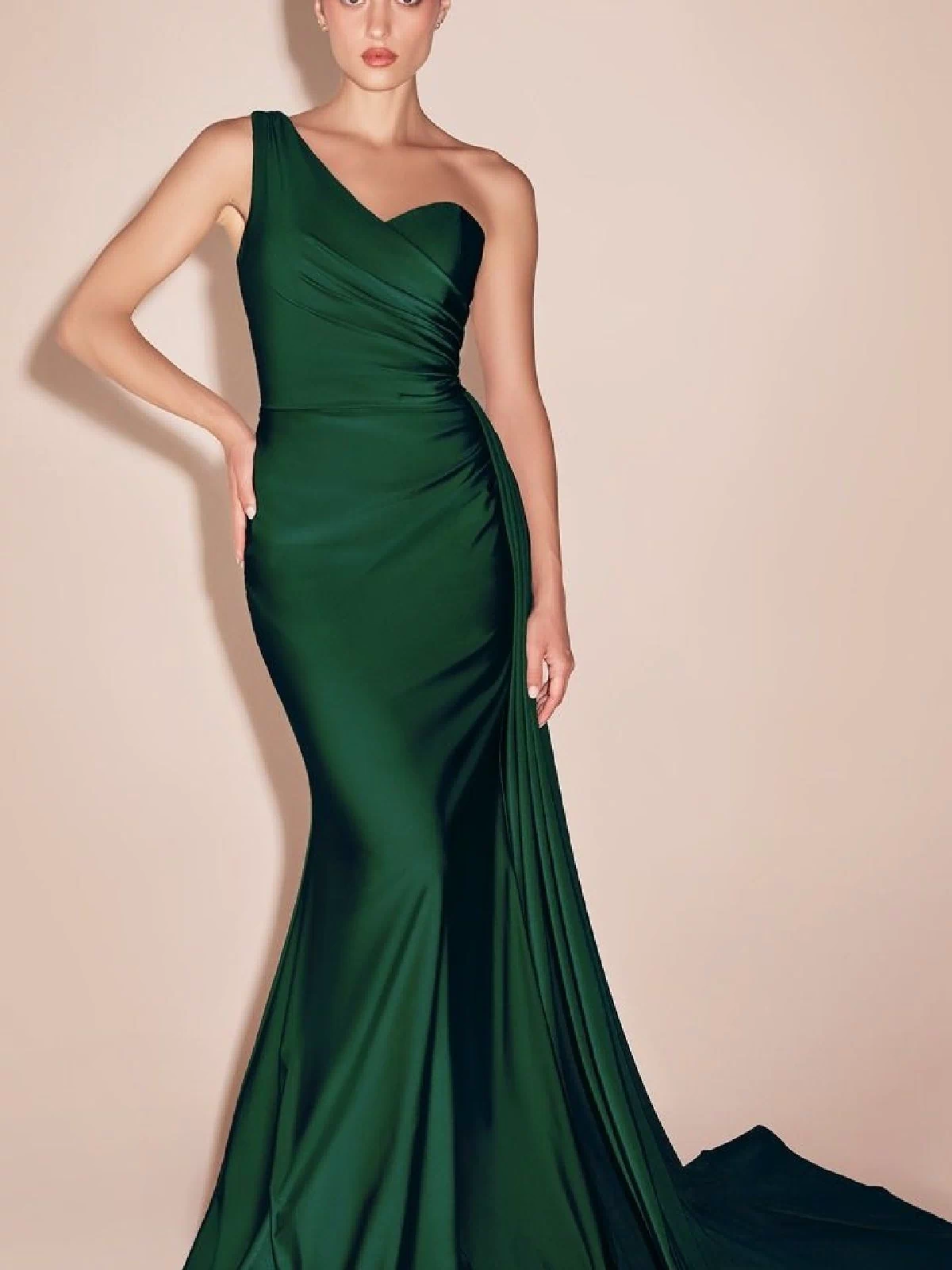 Woman modeling the Side-Sash One-Shoulder Long Prom Dress PT004 in dark green, featuring a fitted floor-length silhouette and slight train, standing against a plain beige background.