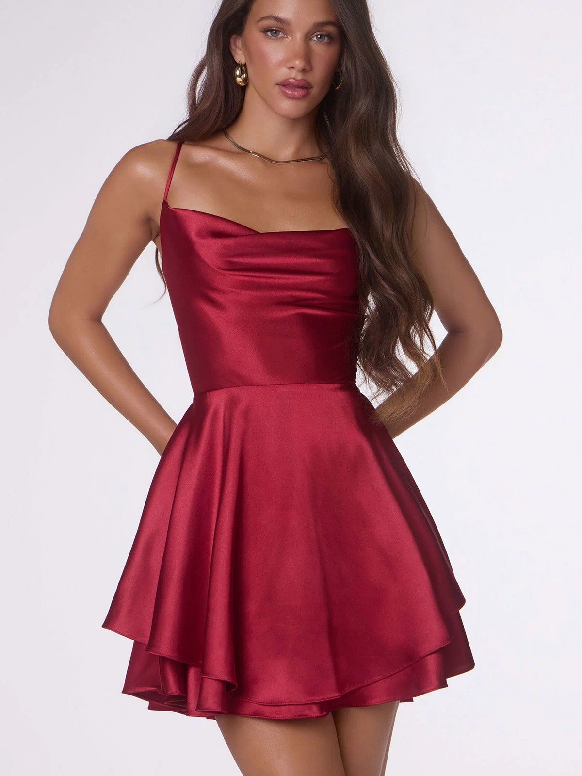 A woman wearing the Short Homecoming Dress: Amoris T616 in burgundy, featuring a sleeveless satin design, cowl neckline, open back, and flared A-line skirt, stands against a plain light background.