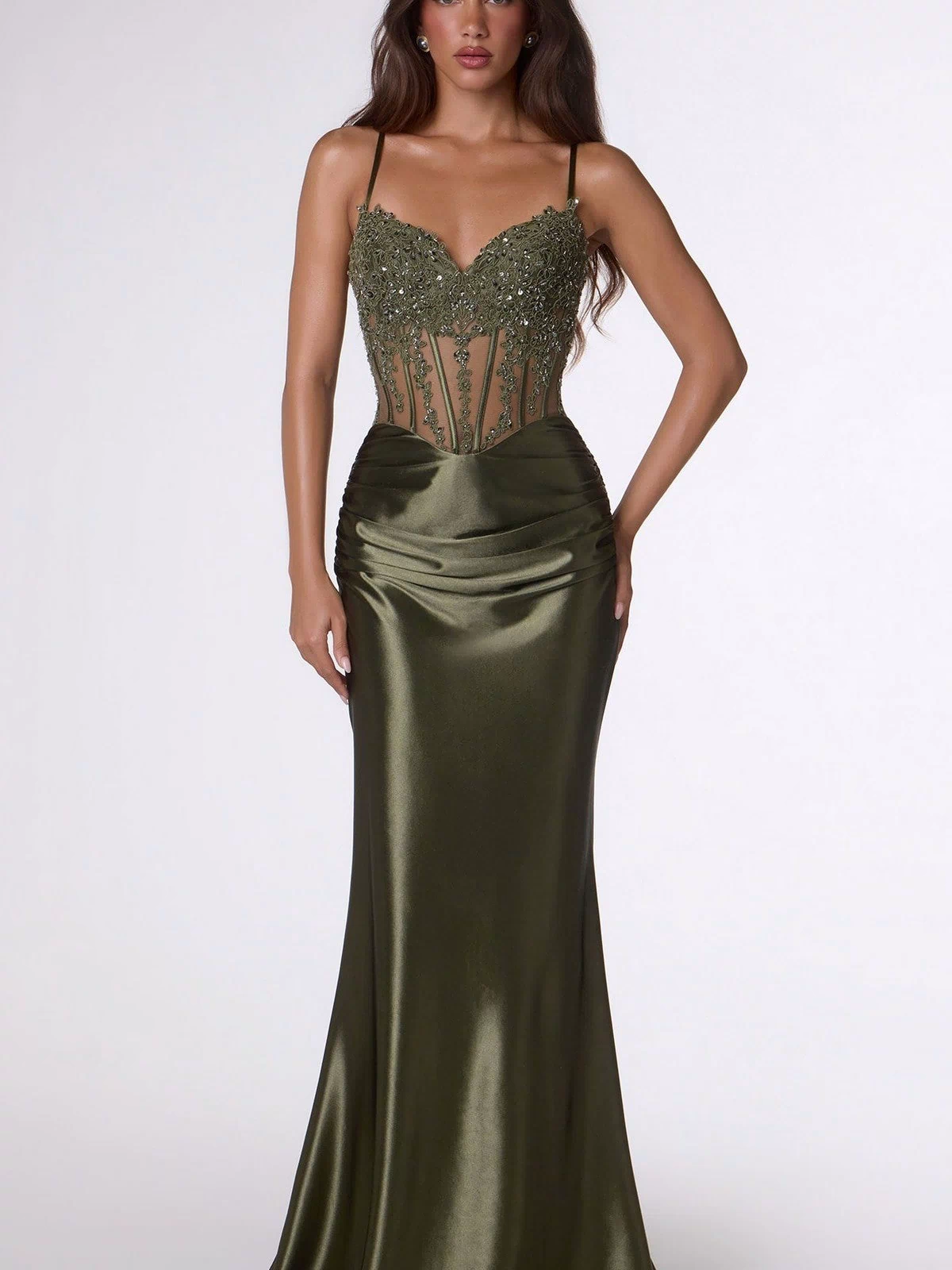 A woman wears the Lace-Up Long Corset Prom Dress: Amoris T819 in olive, featuring a beaded sheer corset bodice and satin skirt, standing against a plain light background.