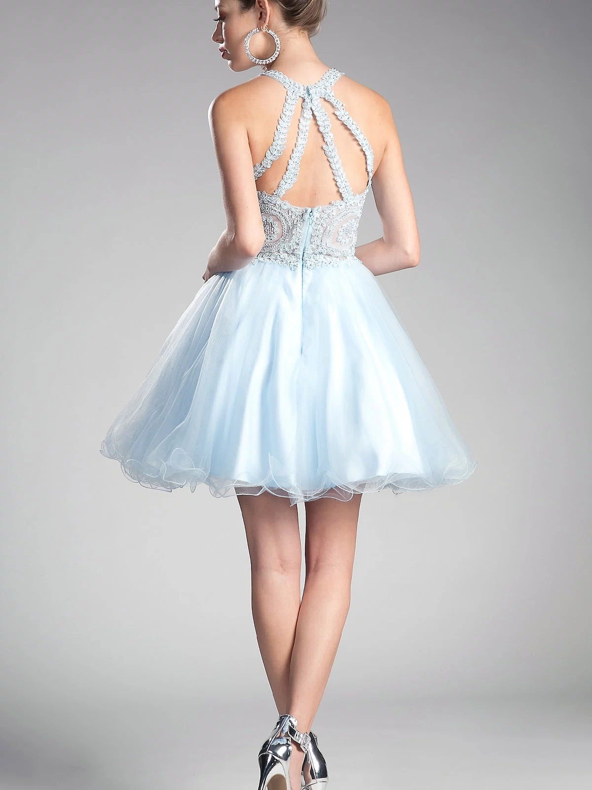 Woman in the High-Neck Short Babydoll Homecoming Dress UJ0119, featuring an embroidered-lace bodice and strappy back, styled with large hoop earrings and silver heels, poses against a plain background.