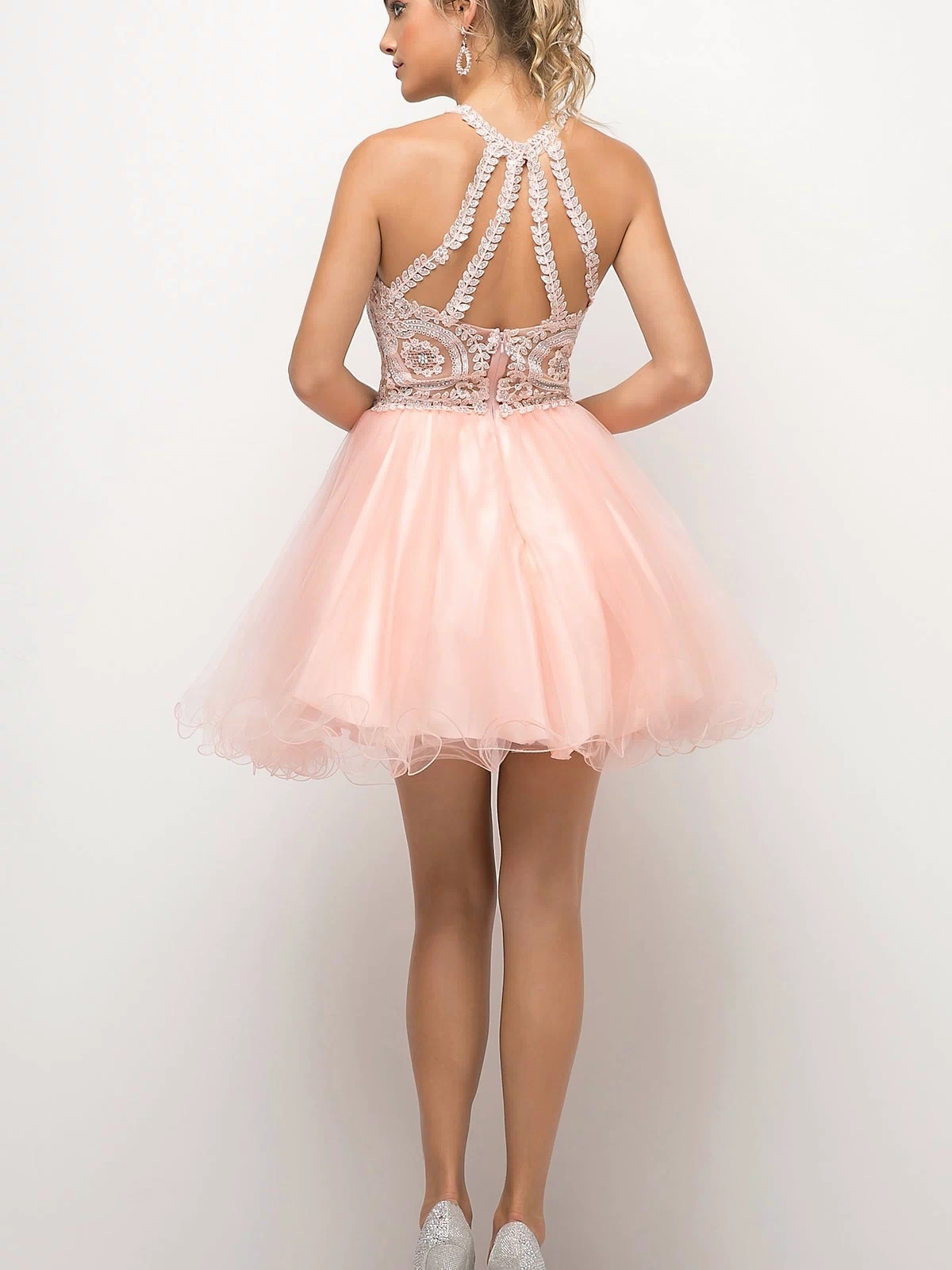 A woman faces away, modeling the affordable High-Neck Short Babydoll Homecoming Dress UJ0119 with a pale pink tulle skirt and embroidered lace bodice, paired with silver heels against a plain white backdrop.