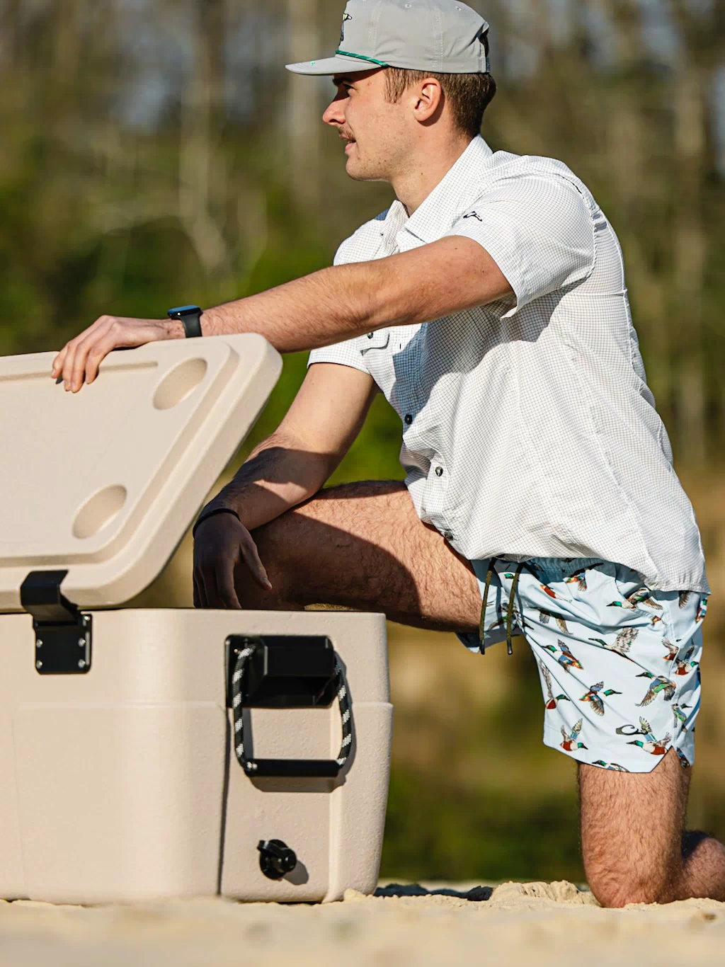 Man kneeling on sandy shore wearing Lake Shore Dock Short, showcasing its water-repellent, stretchy design with elastic waistband, ideal for water-ready adventures.