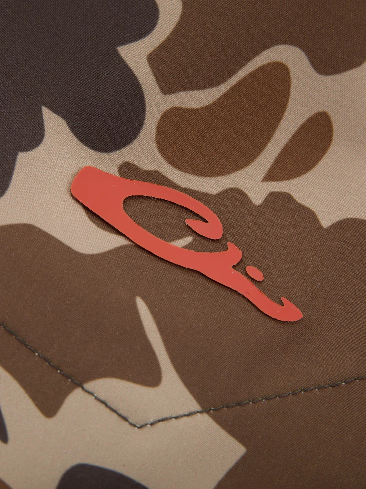 Close-up of the Lake Shore Dock Short's desert-camo fabric with a red emblem, showcasing its durable stitching and lightweight, water-repellent design for outdoor comfort.