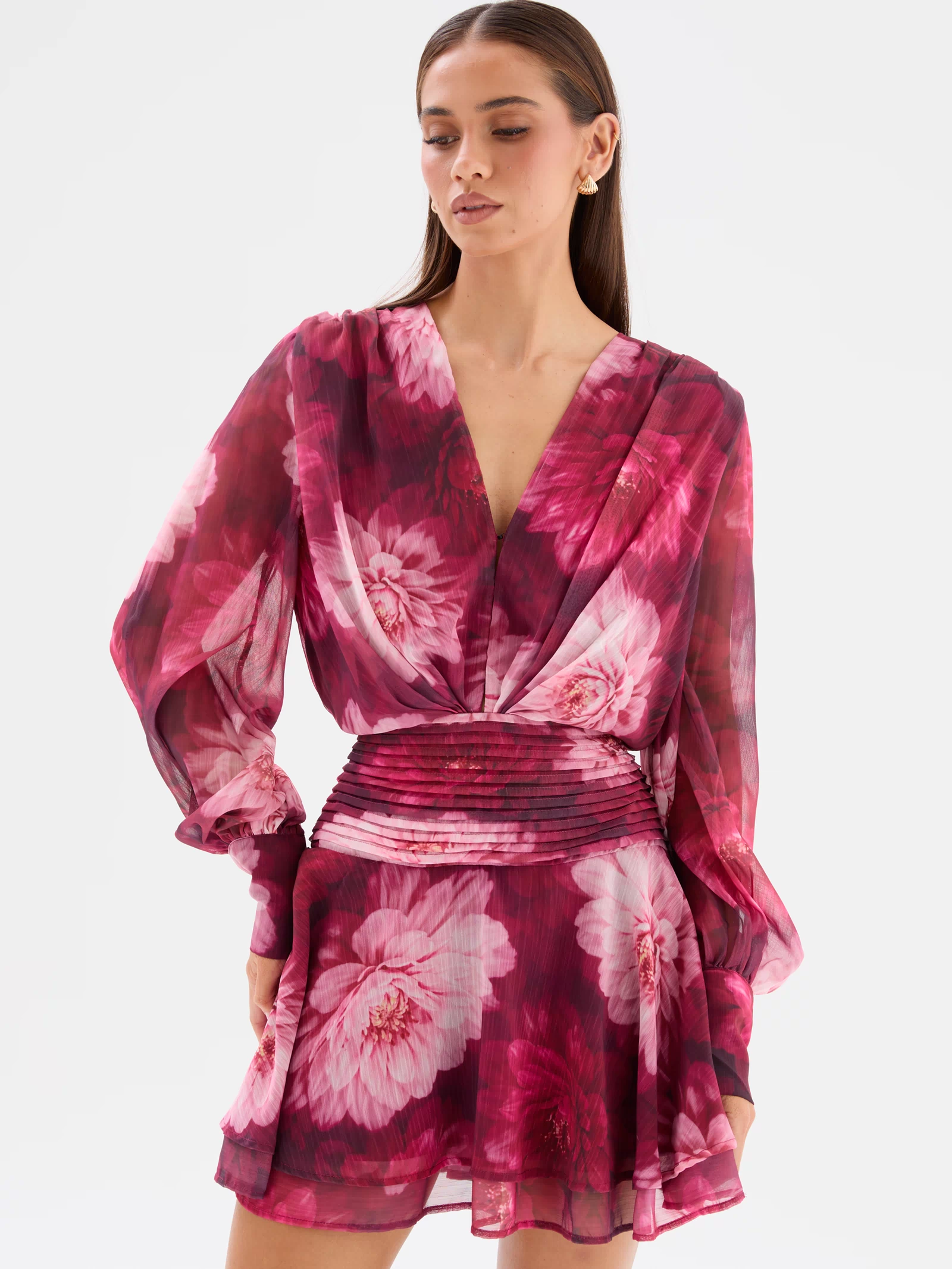 Close up front view: Lanarah Mini Dress in Ruby Dahlia with a plunging V-neckline, draped bodice, long sheer blouson sleeves, fitted pleated waistband and flowing mini-length silhouette.
