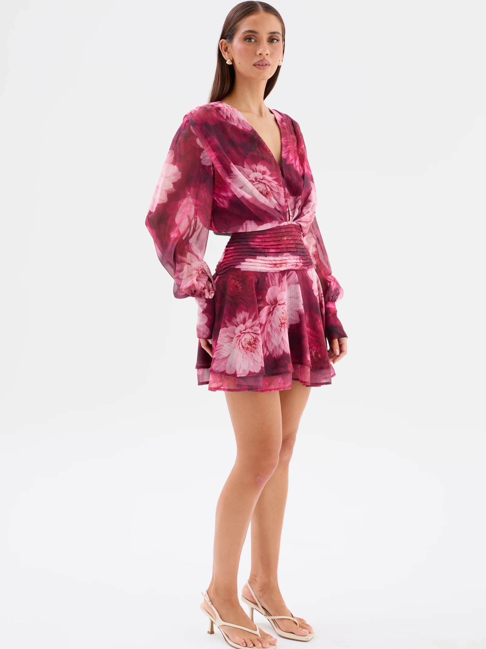 Full side view: Lanarah Mini Dress in Ruby Dahlia with a plunging V-neckline, draped bodice, long sheer blouson sleeves, fitted pleated waistband and flowing mini-length silhouette.