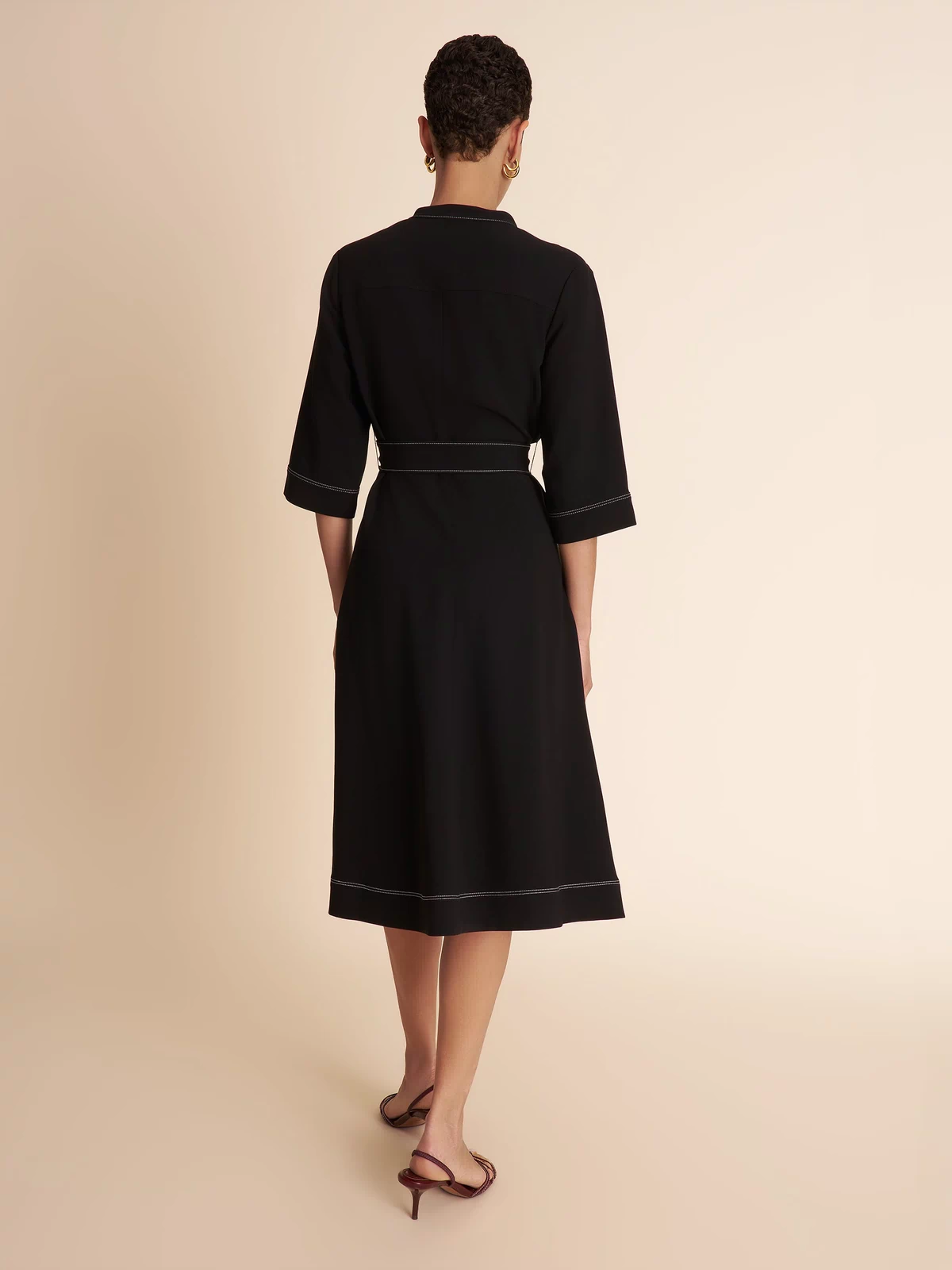 Woman wearing a black dress with a belt on a beige background