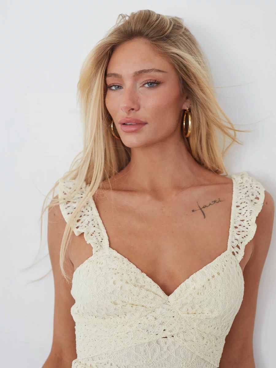 Woman wearing a white crochet dress against a plain background