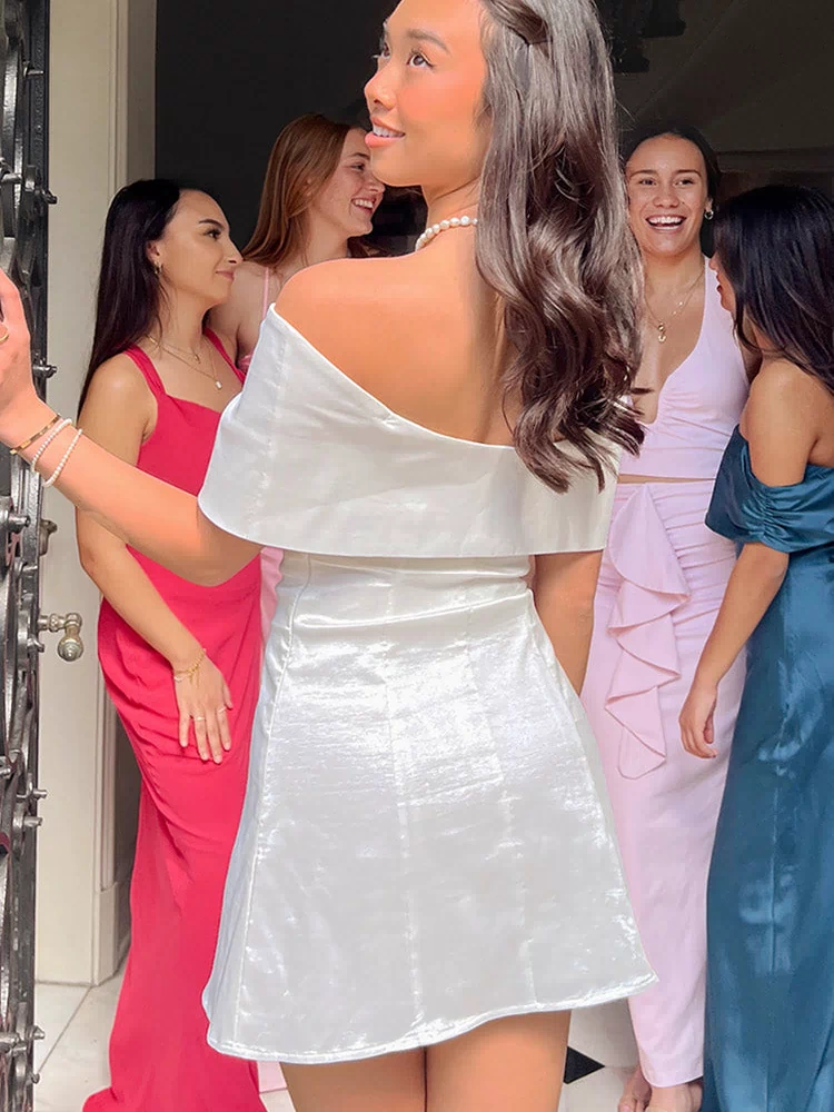 Back view of a white off-shoulder mini dress with a wide flounce neckline and shimmery A-line skirt