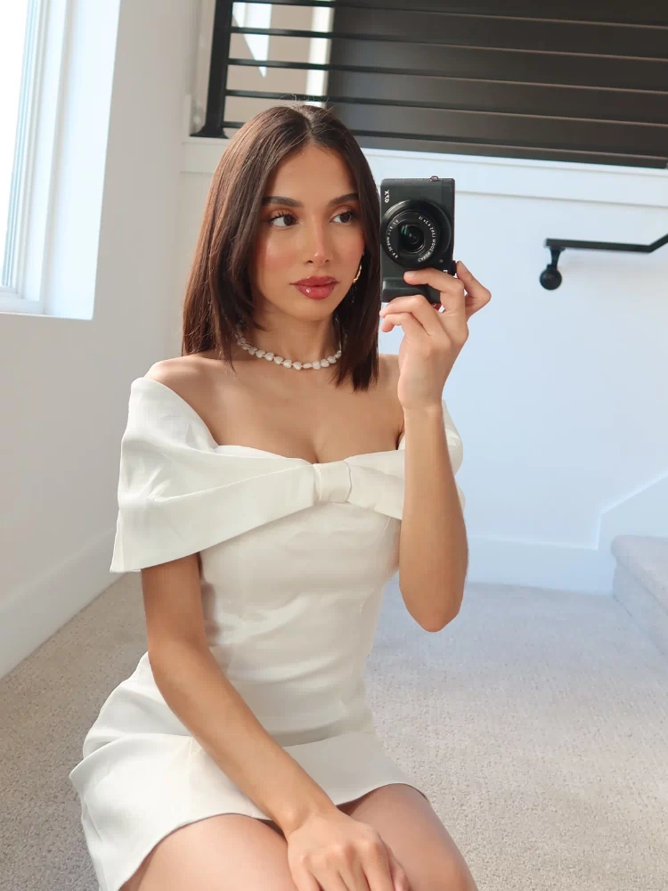 Close-up of the white off-shoulder mini dress showing the large bow detail at the bust