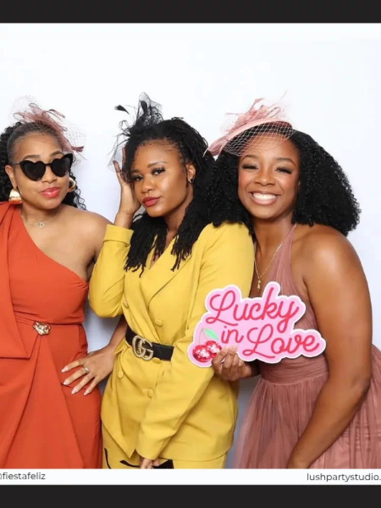 Three women posing together with a 'Lucky in Love' wedding prop sign