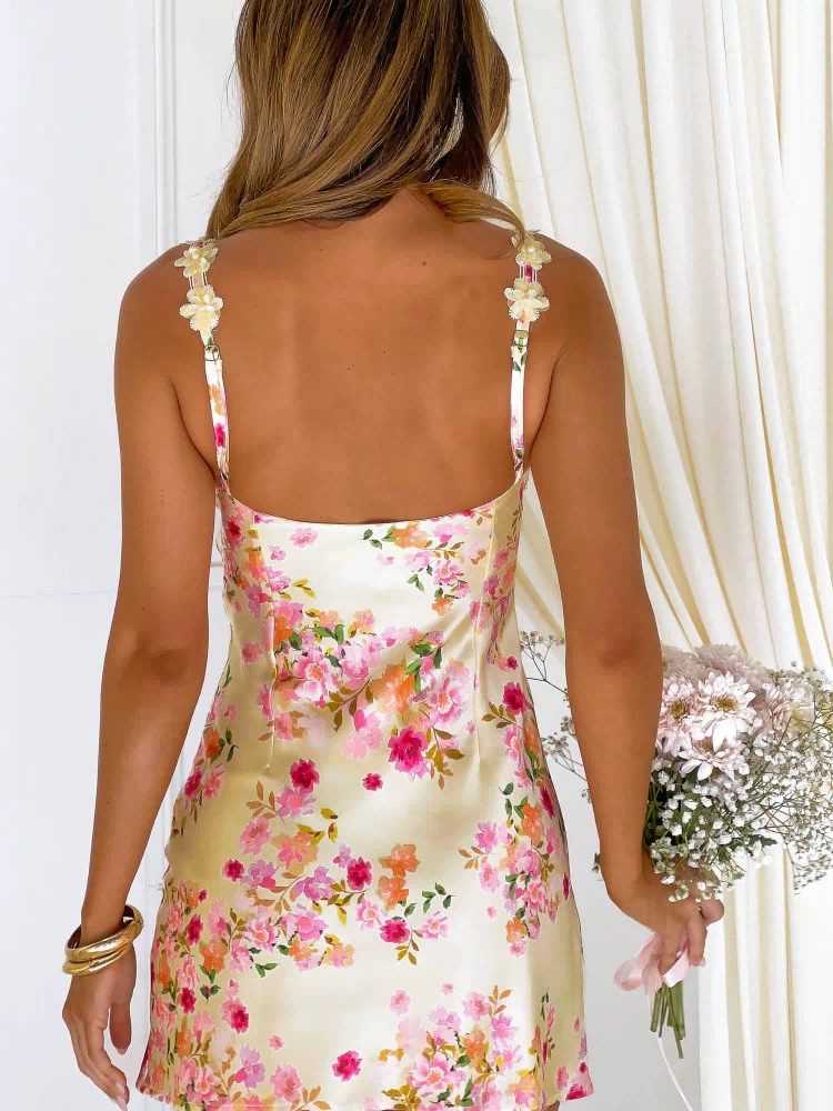 Rear view of a yellow floral satin mini dress with a square back and decorative flower appliques on the spaghetti straps
