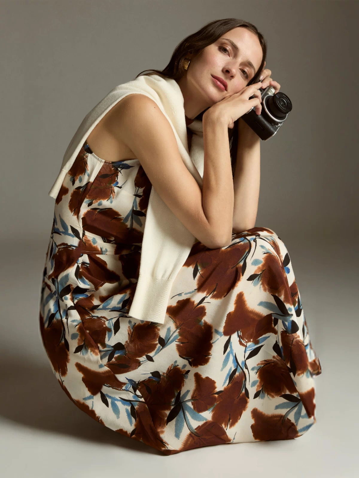 Woman in a floral dress holding a camera against a neutral background