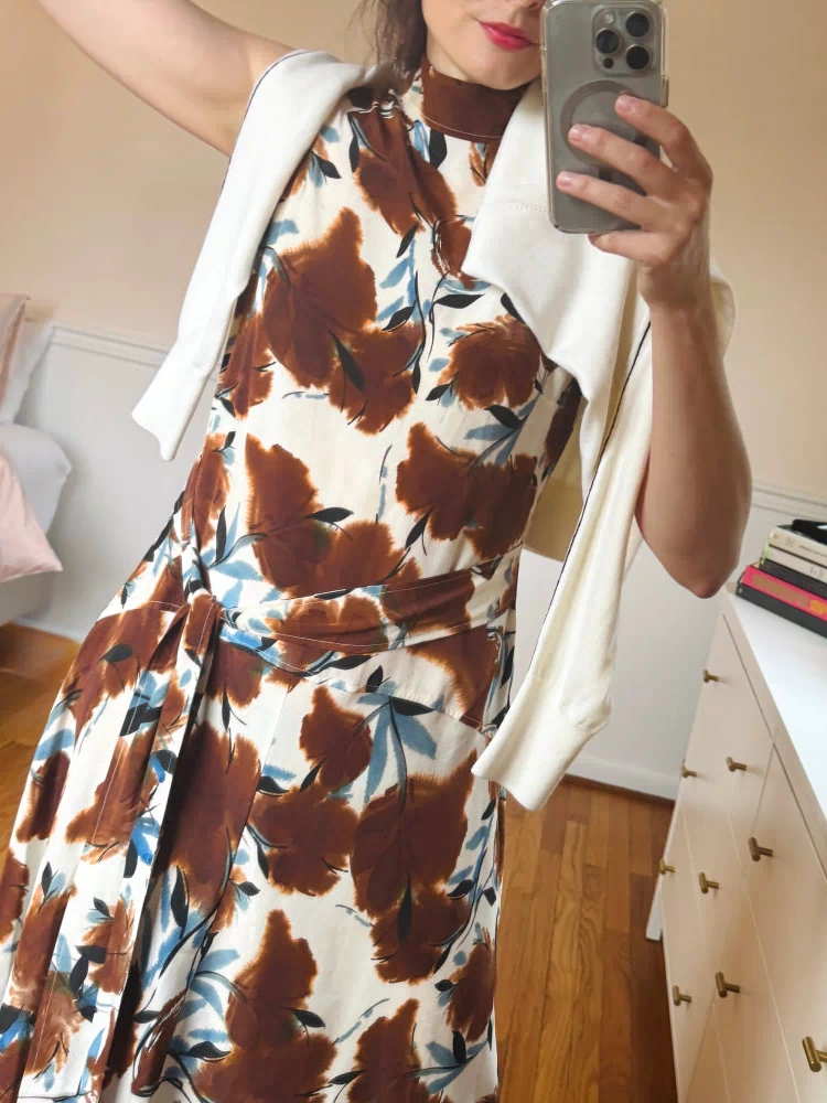 Person wearing a floral dress with brown and blue patterns in a bedroom setting.