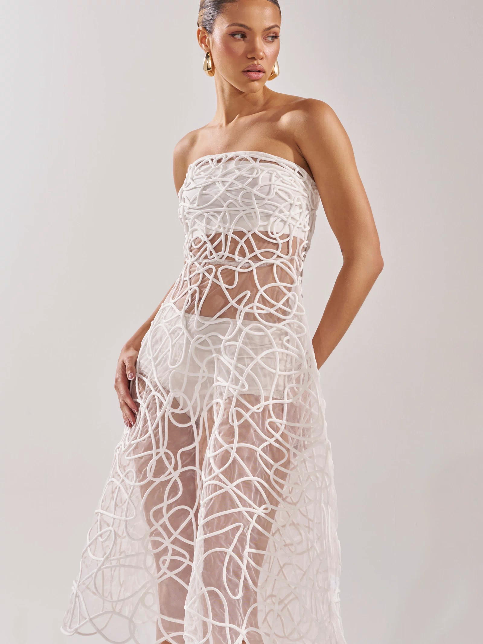 The MAYA ABSTRACT MIDI DRESS IN WHITE features a strapless sheer midi silhouette with swirling abstract lines over a short white underlay—an elegant pick for any cocktail party.