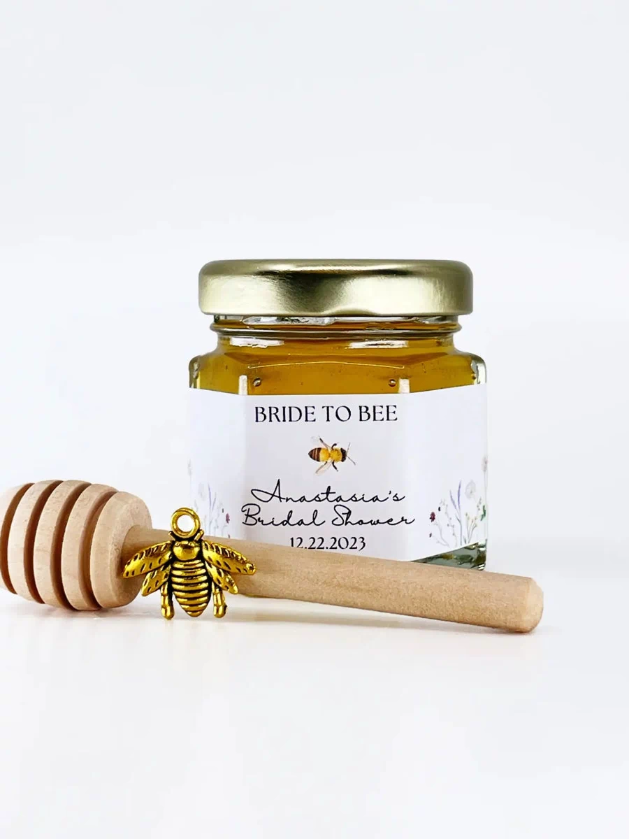Jar of honey with a gold lid and wooden honey dipper on a white background, featuring 'Bride to Bee' branding.