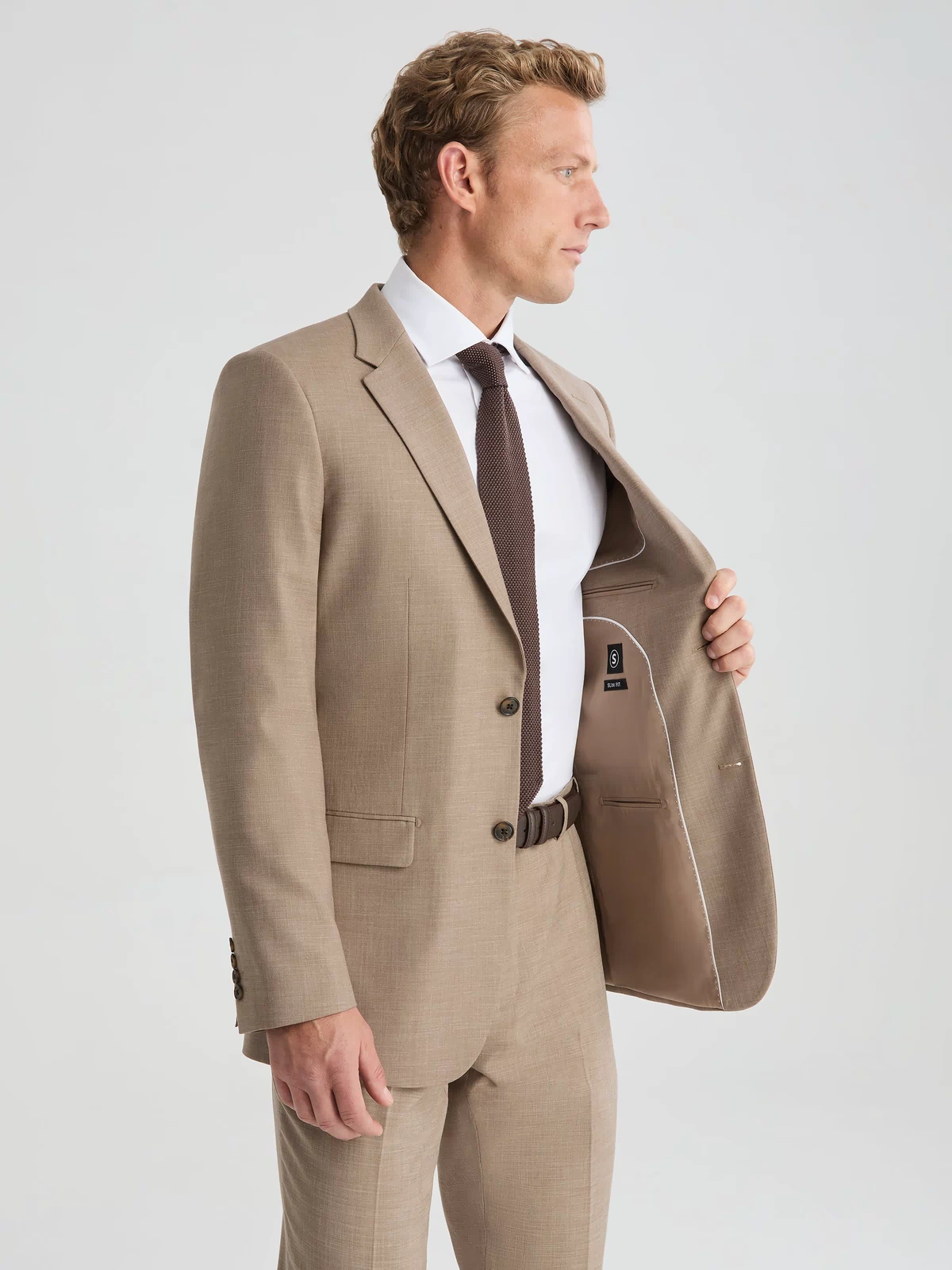 Man wearing dark tan suit jacket and suit pants. Paired with white long sleeve button up shirt and dark brown tie.