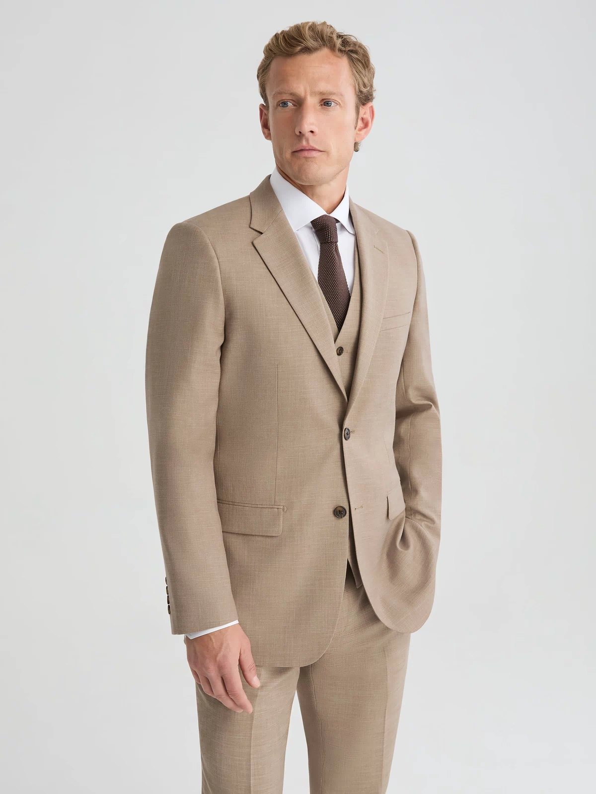 Man wearing dark tan suit jacket and suit pants. Paired with dark brown vest, white long sleeve button up shirt and dark brown tie.