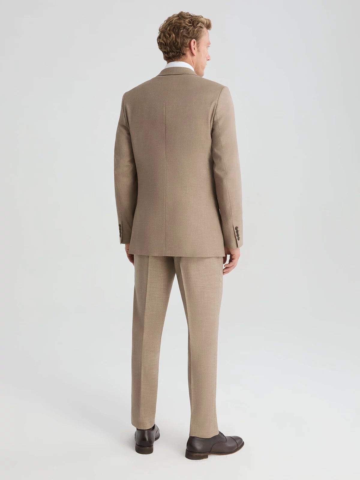 Back view of man wearing dark tan suit jacket and suit pants. Paired with white long sleeve button up shirt and dark brown tie.