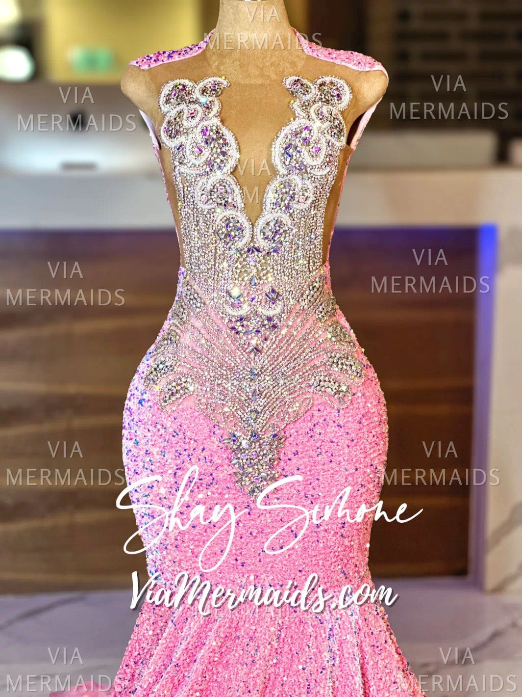An image of a mannequin wearing a floor-length iridescent pink sequin mermaid gown with intricate rhinestone details.